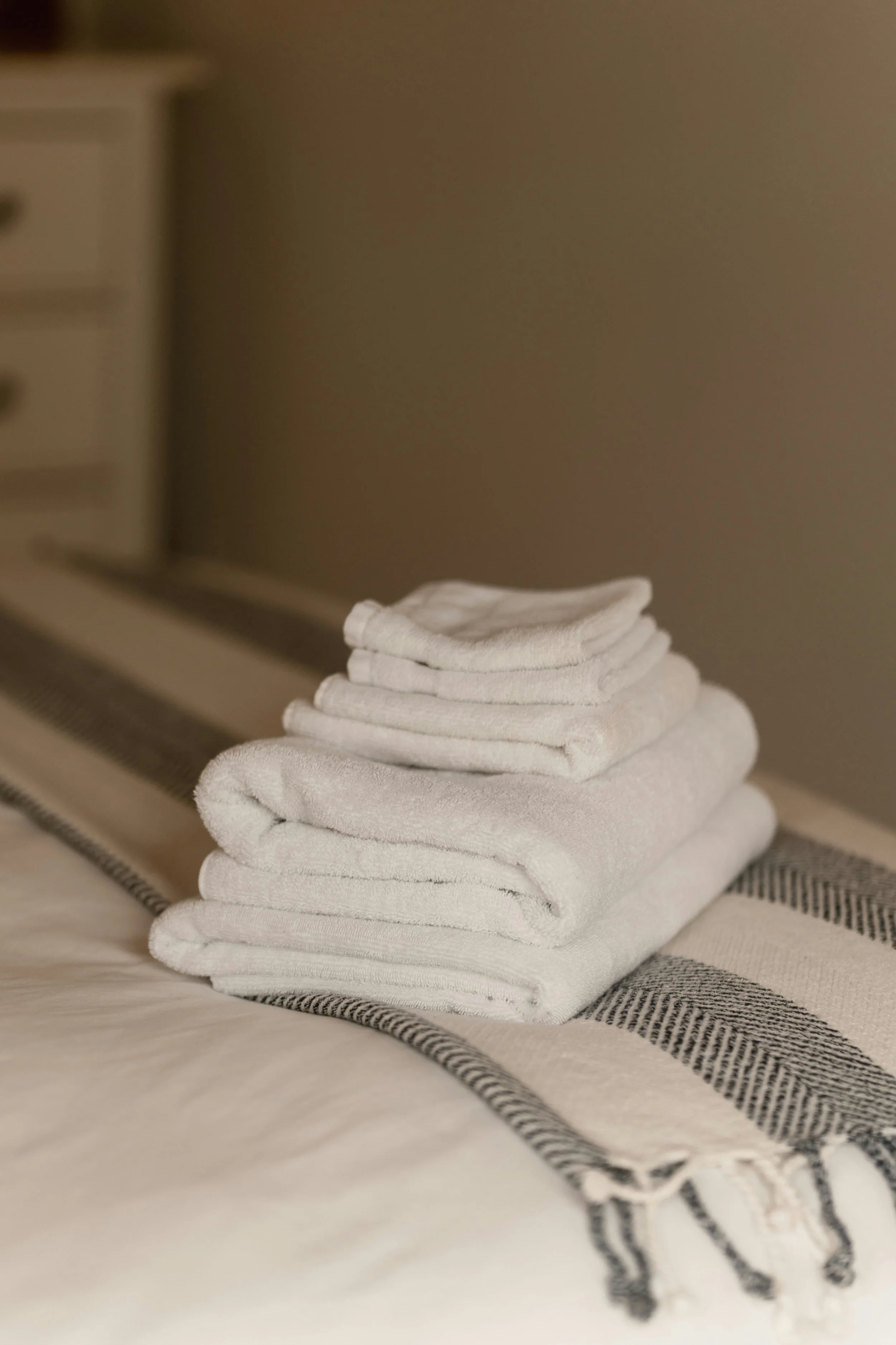 Stack of folded white towels on a bed with a striped blanket.