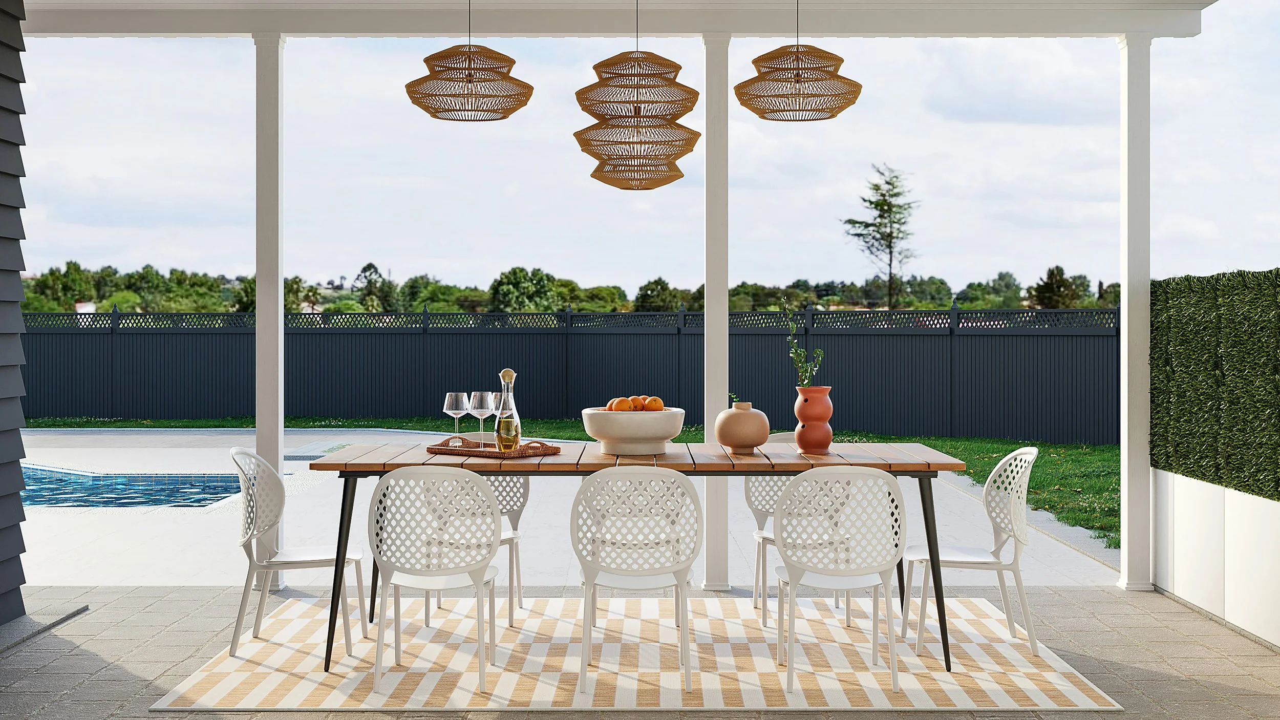 Outdoor patio with a wooden dining table, six white chairs, three woven pendant lights, and a view of a backyard with a pool and green fencing.