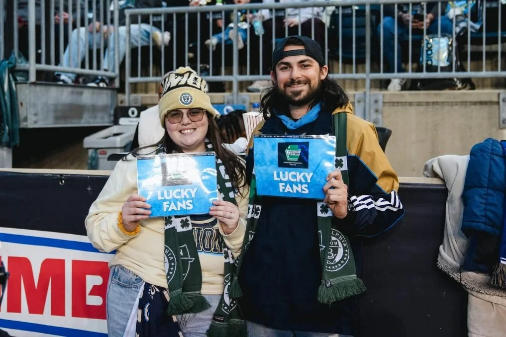 Two smiling fans in stadium holding signs that say 'Lucky Fans'.