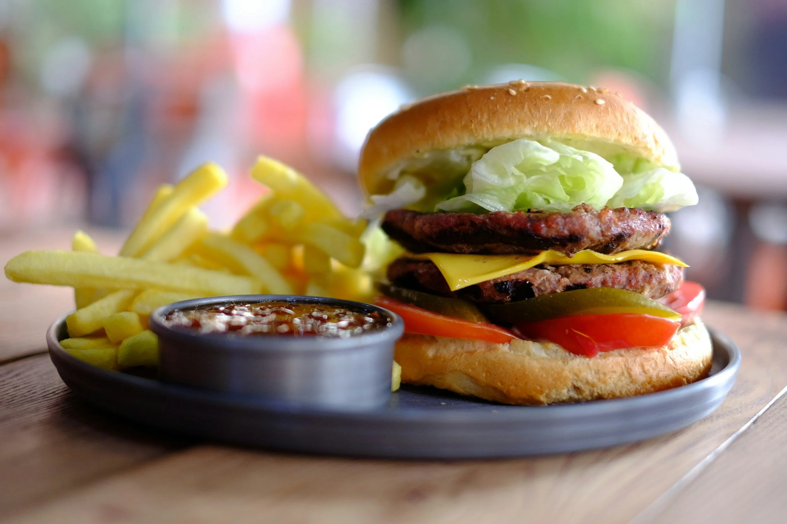 A plate with a cheeseburger, French fries, and a side of barbecue sauce.