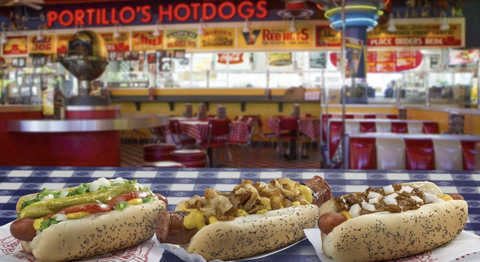 Three hot dogs with various toppings on a checkered paper at a classic American diner restaurant.