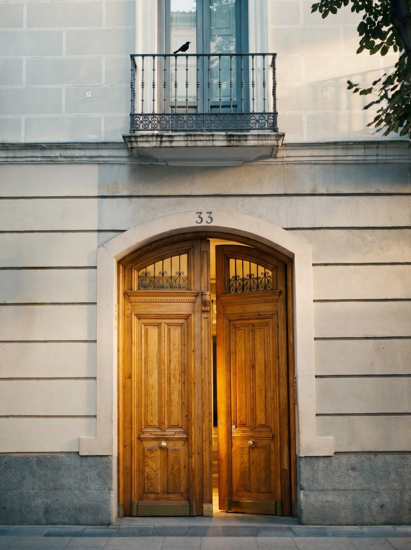 Puerta de madera con arco en un edificio con fachada de piedra y balcón con barandilla de hierro, número 33.