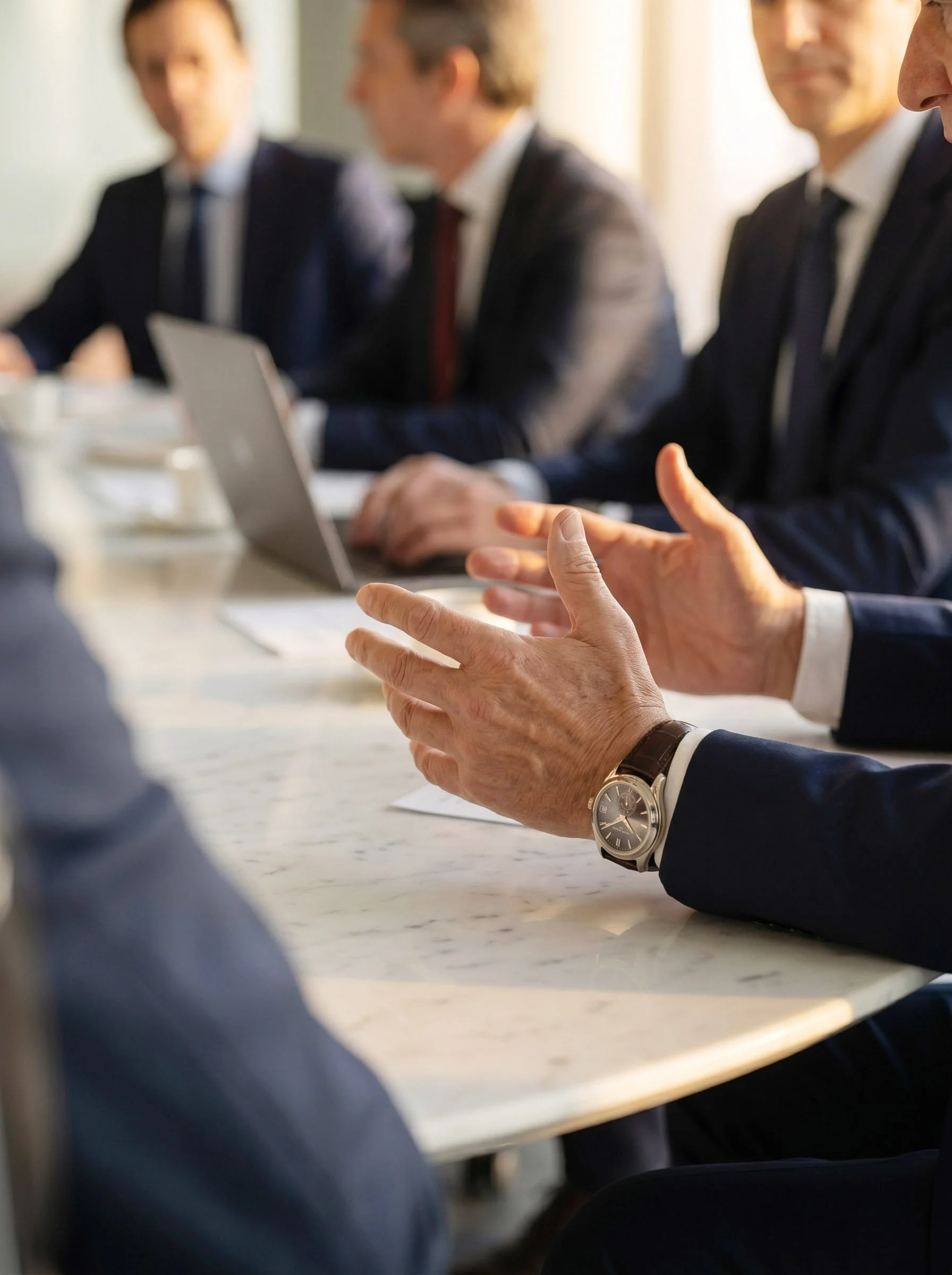 Hombres de negocios en traje sentados en una mesa de conferencia, algunos con laptops, participando en una reunión.