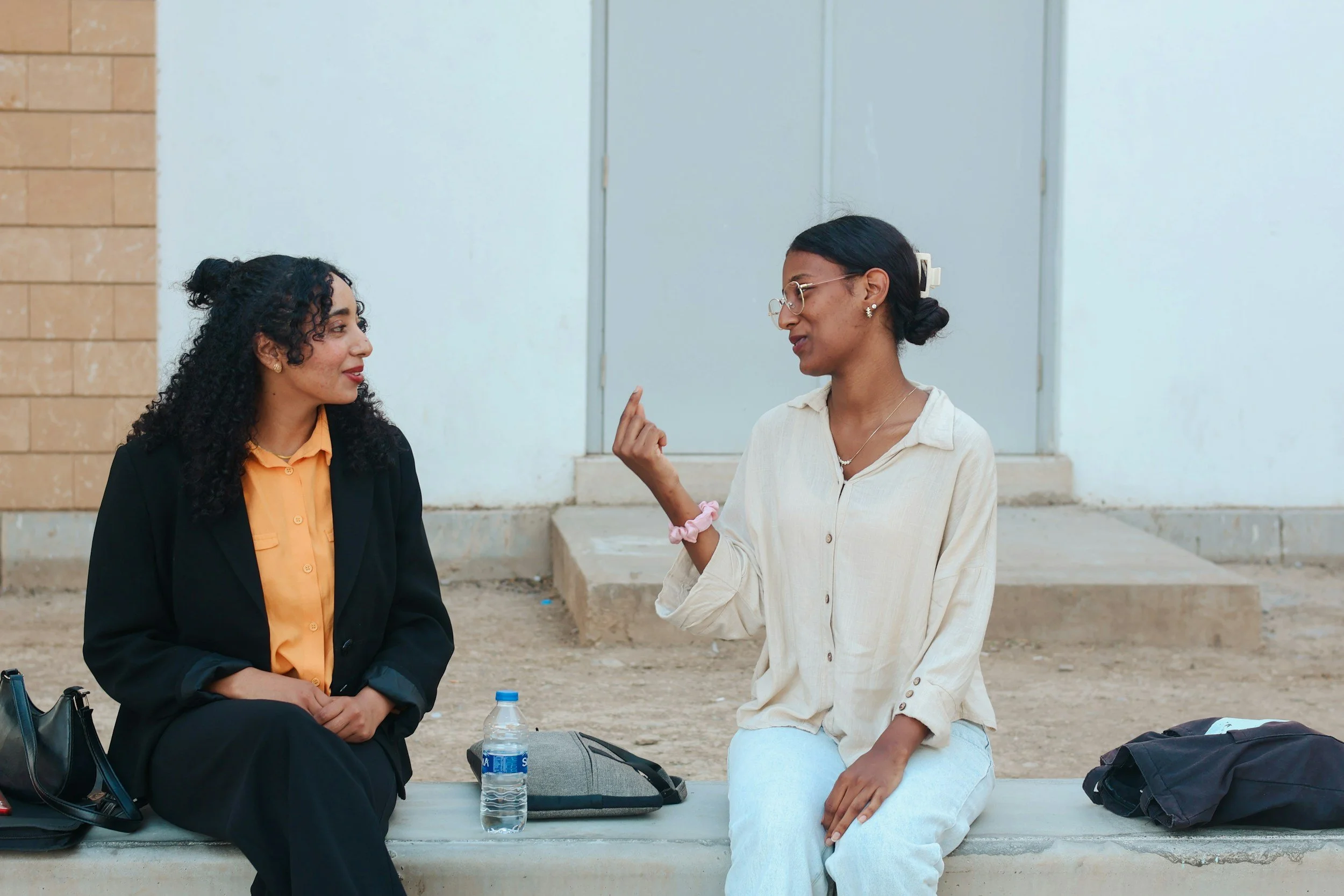 Two women having a conversation at a conference table in a modern office with a brick wall background.