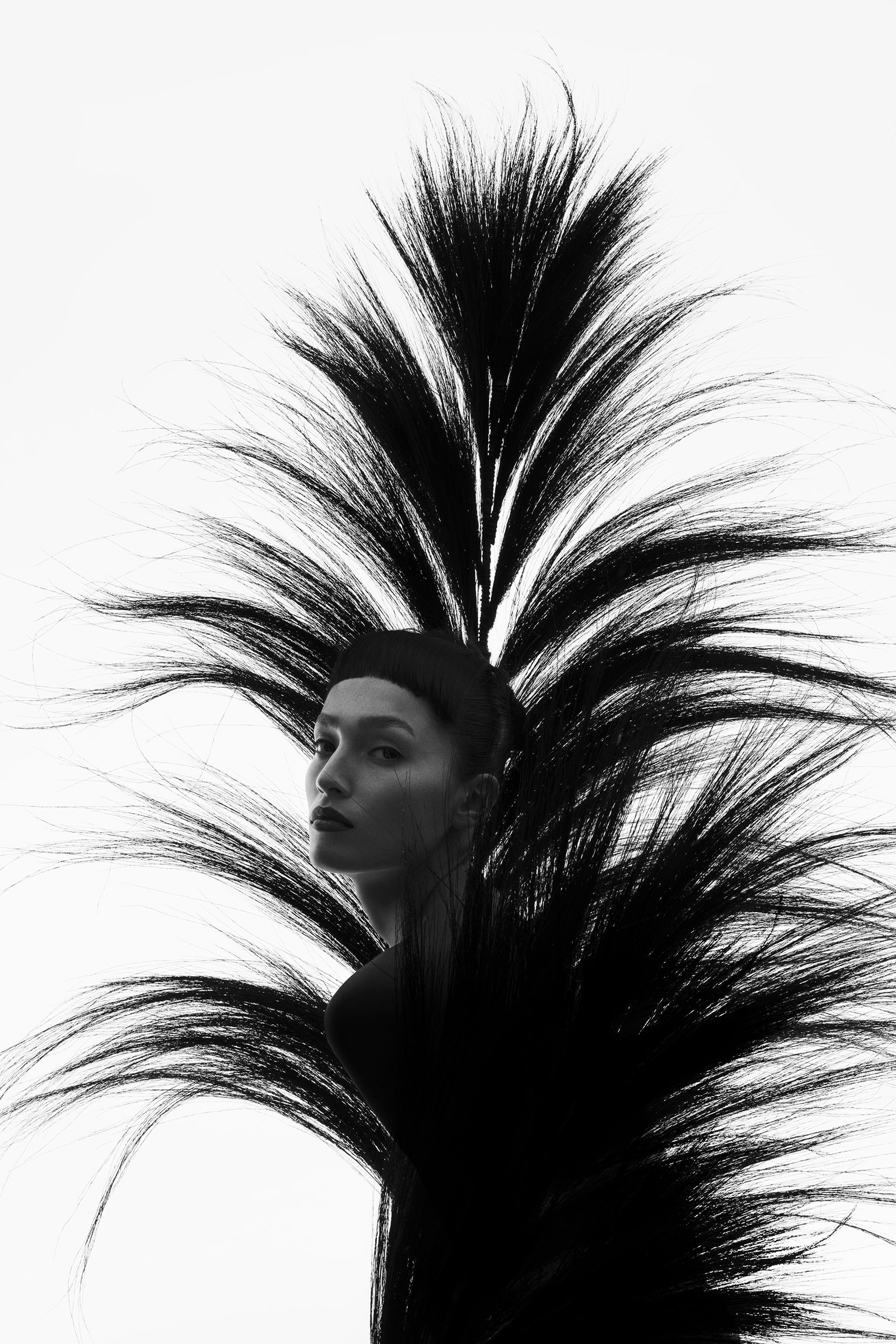 Black and white photo of a woman with tall, dramatic hairstyling that extends outward in multiple wispy, spiky directions, framing her face with an artistic and avant-garde appearance.