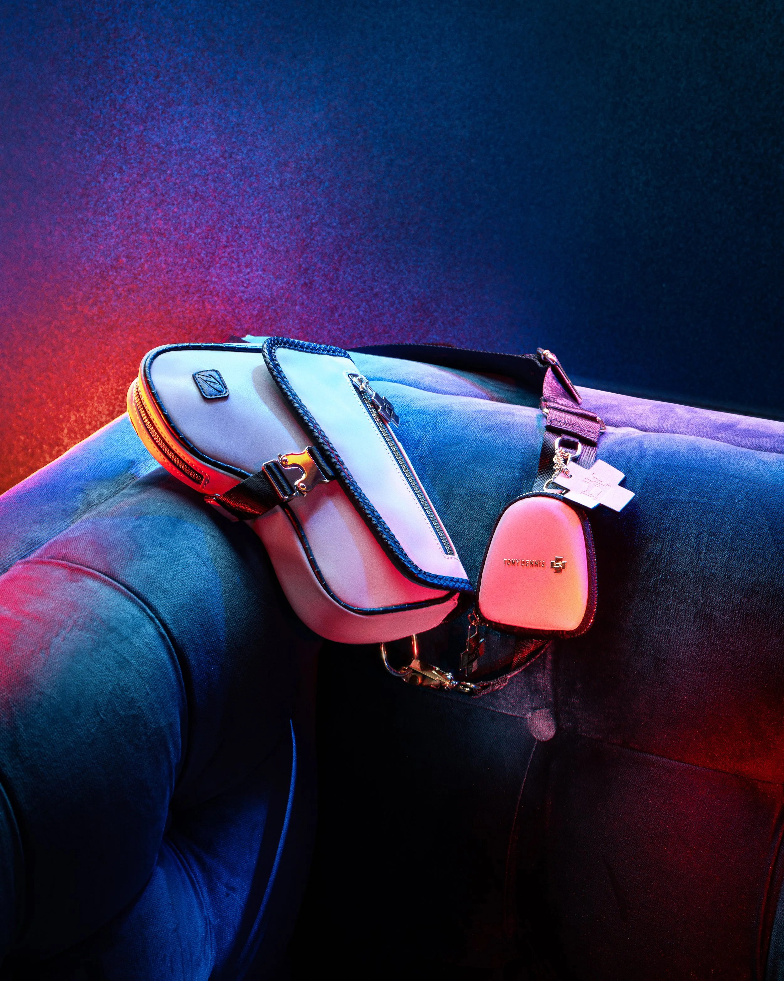 Person sitting on a dark couch with neon lighting, holding a white and black designer bag with the brand name Tony Dennis and a keychain attached.