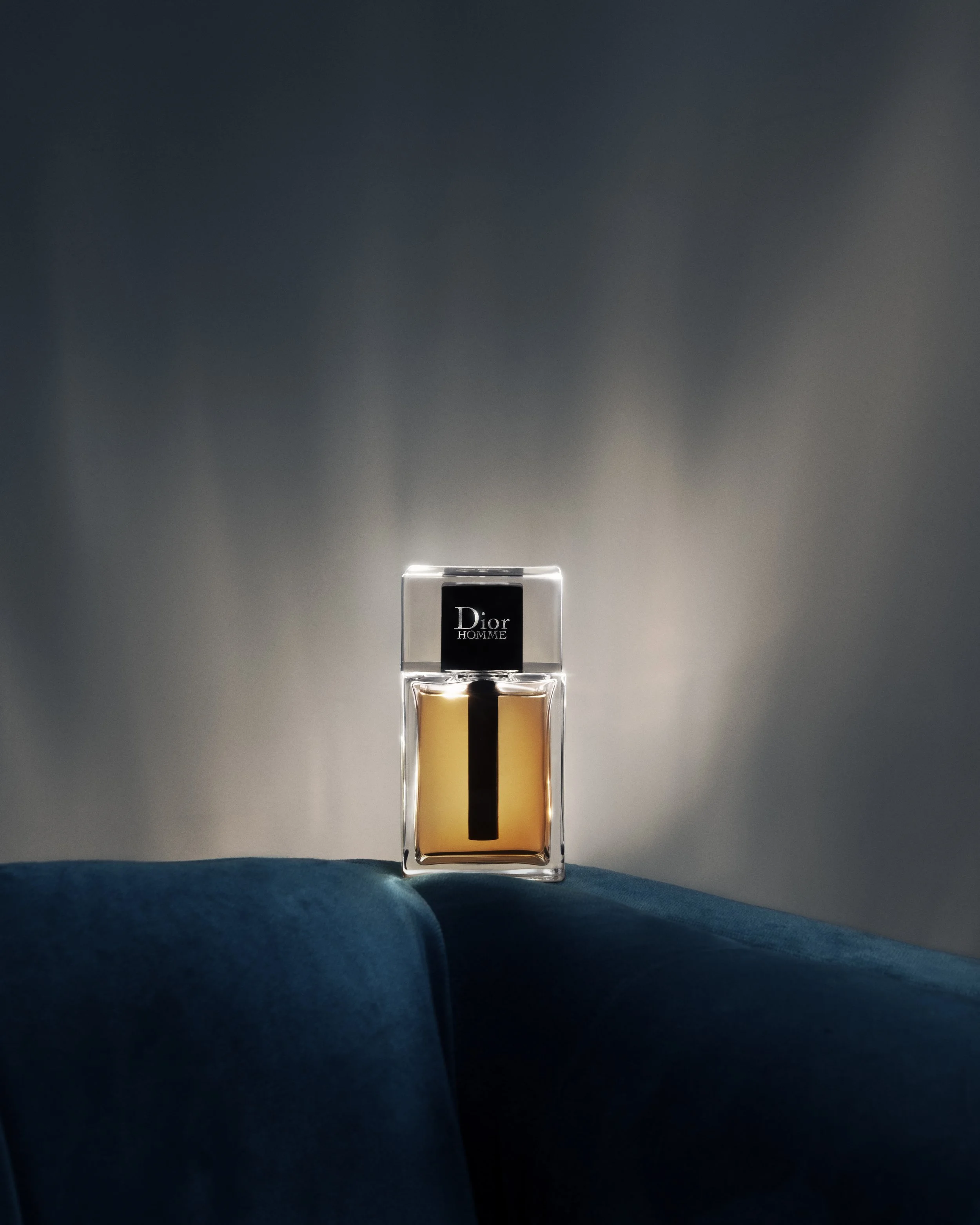 A bottle of Dior Homme perfume on a dark background with spot lighting.