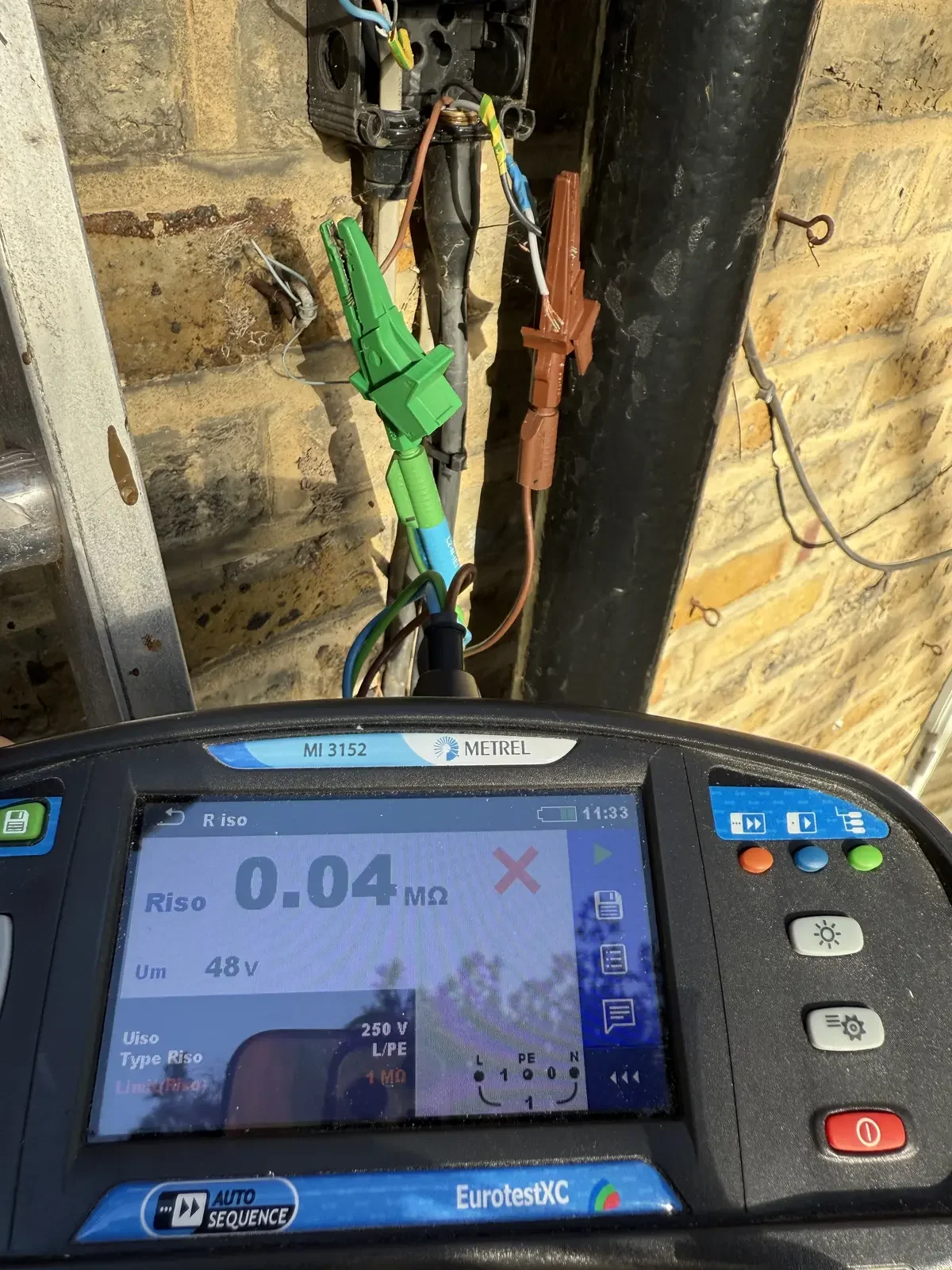 Electrical testing device showing a very low resistance reading of 0.04 ohms in front of exposed electrical wires and connectors on a wall.