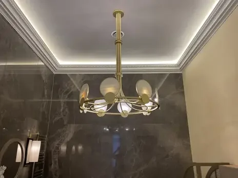 Modern chandelier with multiple white globe lights hanging from a gold fixture, mounted on a ceiling with crown molding in a room with dark marble walls.