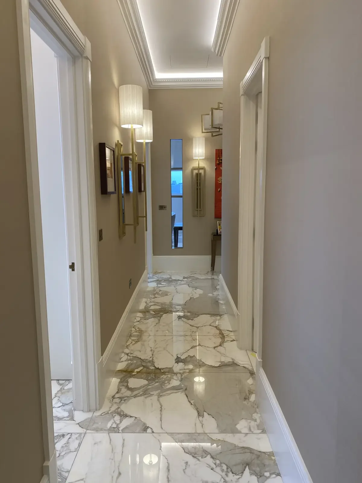 Luxurious hallway with polished marble flooring, fluted wall lights, and concealed ceiling LED strips creating soft, continuous ambient light. High-end electrical install.