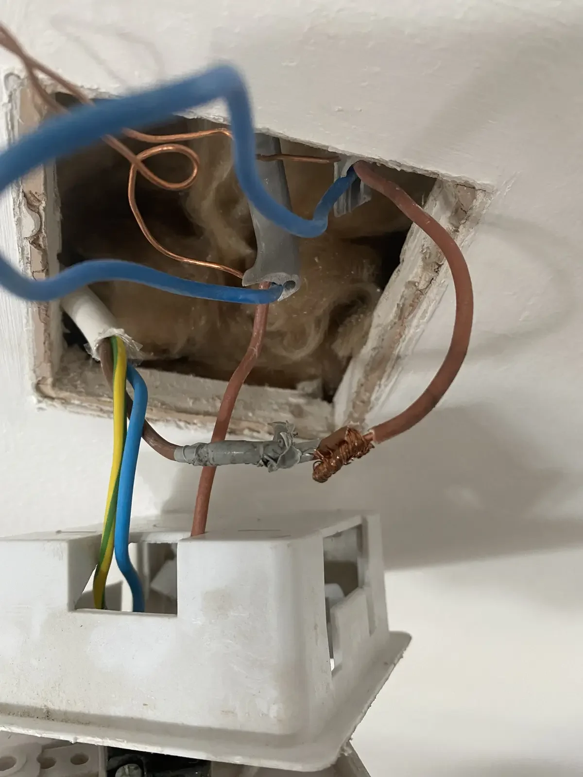 Inside an electrical box with blue, brown, white, yellow, and green wires exposed and connected, with some copper and metal components visible.