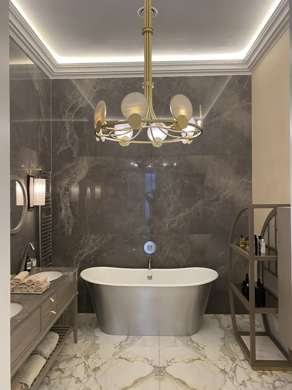 Luxurious bathroom with gold chandelier, marble walls and flooring, and concealed LED lighting around the ceiling perimeter for a refined, modern aesthetic.