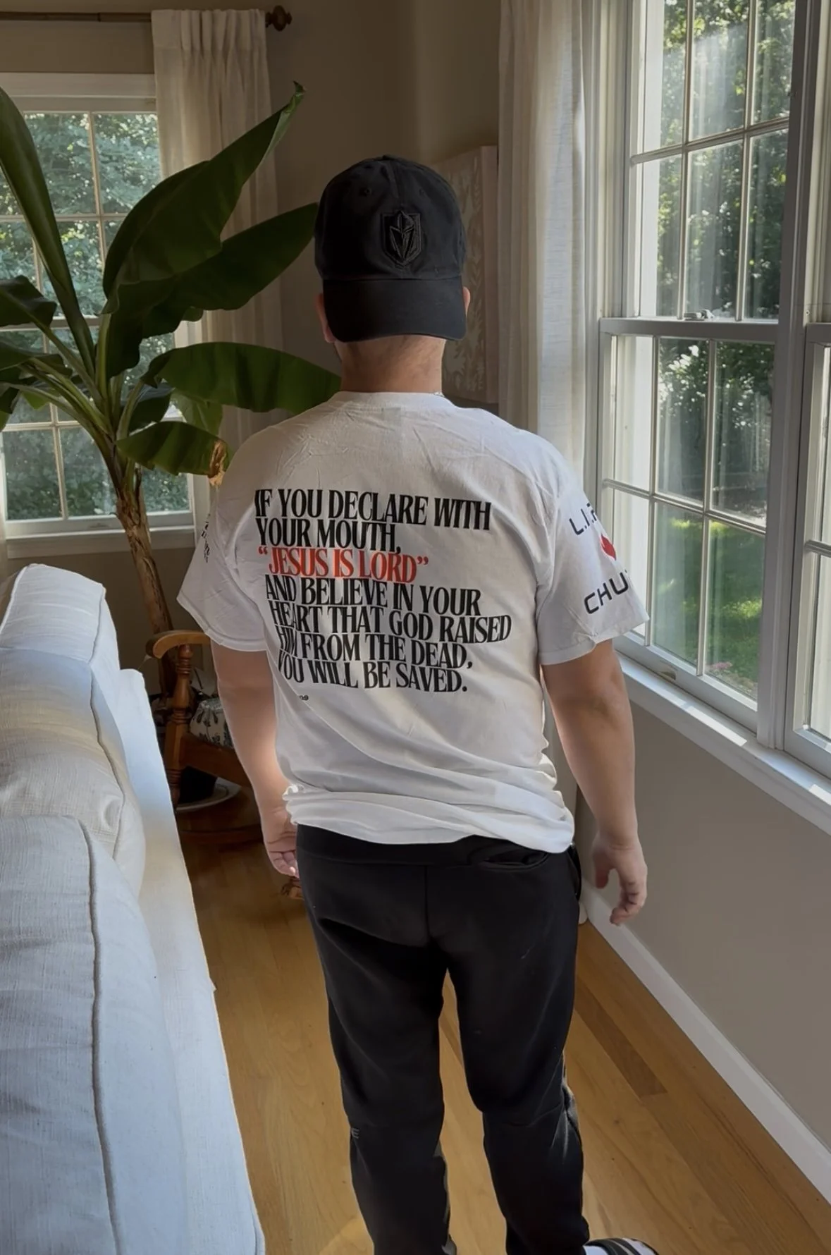 Man wearing a white t-shirt featuring Romans 10:9 Scripture declaring Jesus is Lord, faith-based apparel inspired by the Word of God.