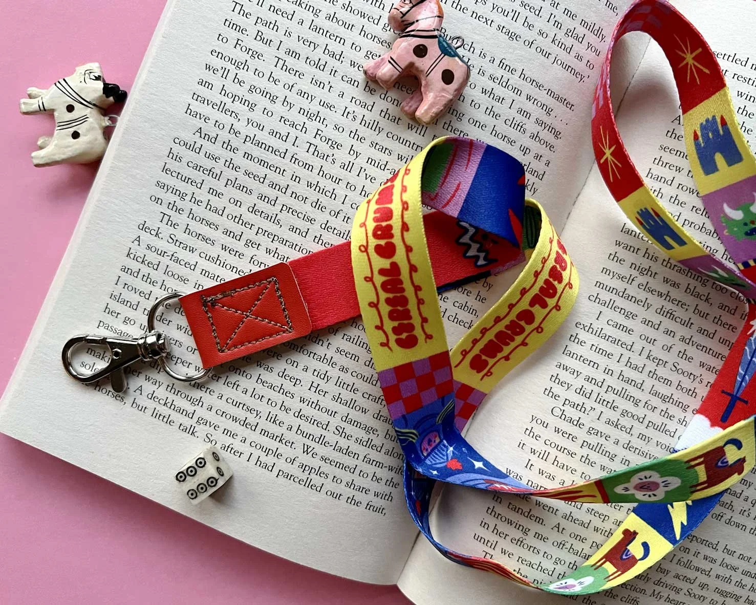 Brightly coloured, fantasy themed lanyard on a pink background. Goblins, kinights, swords and castles adorn a fabric keychain lanyard.