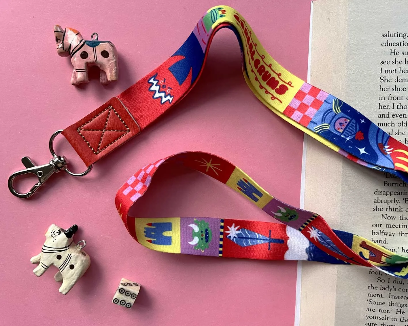 Brightly coloured, fantasy themed lanyard on a pink background. Goblins, kinights, swords and castles adorn a fabric keychain lanyard.