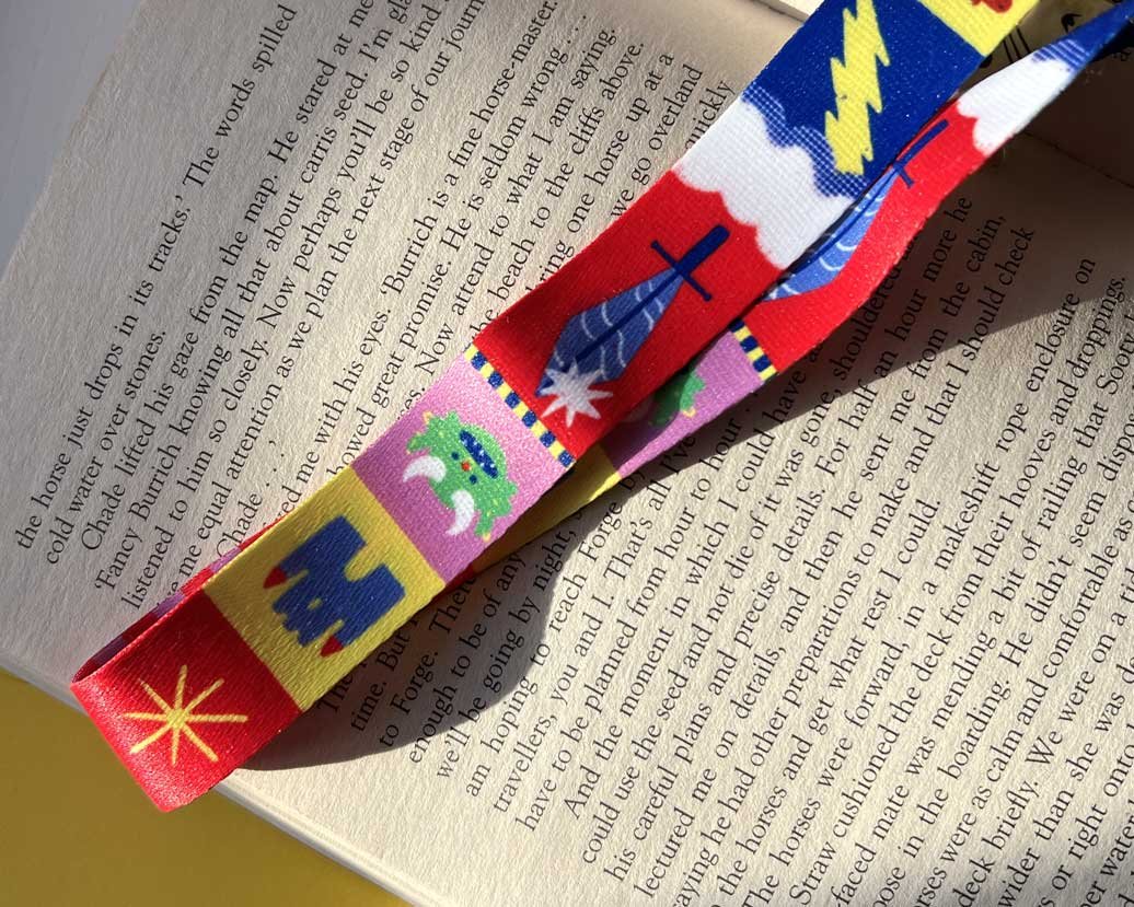 Brightly coloured, fantasy themed lanyard on a pink background. Goblins, kinights, swords and castles adorn a fabric keychain lanyard.