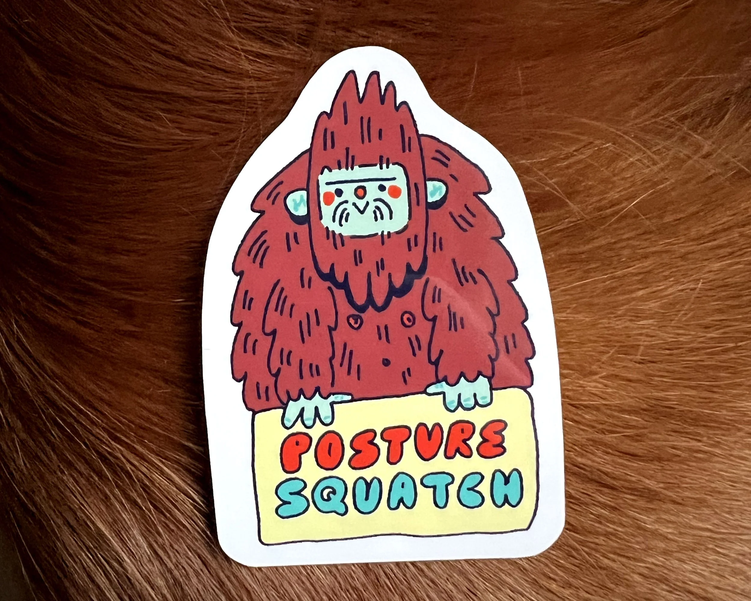 Colorful sticker of a cartoon Bigfoot or Sasquatch with red fur, holding a yellow sign that says 'Posture Squatch' in red and blue letters, on a wooden surface.