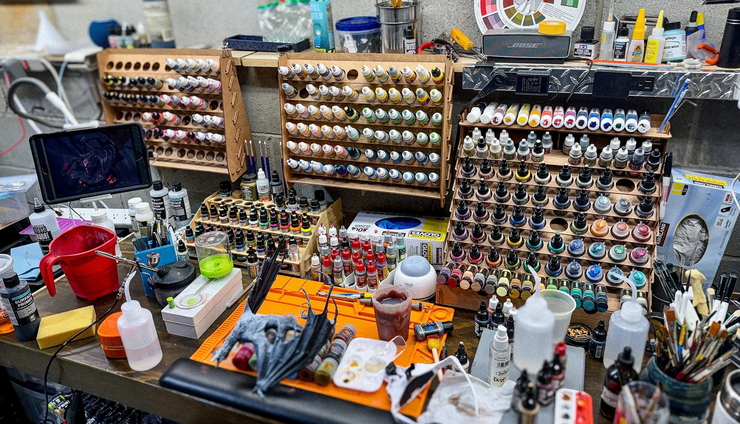 A cluttered workbench filled with paint bottles and painting supplies.