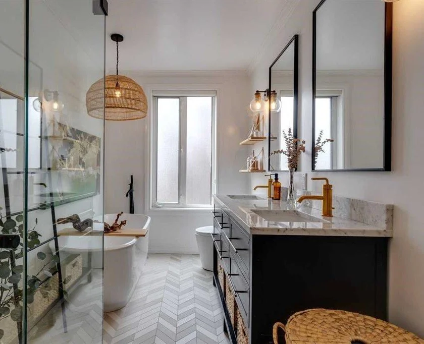 Modern bathroom with a freestanding bathtub, double vanity with gold fixtures, large framed mirrors, and a glass-enclosed shower with greenery decoration.