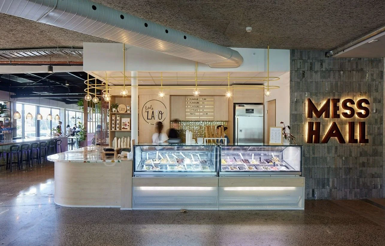 Ice cream shop counter with glass display cases showing various flavors, a sign reading 'Little Lato,' and a large illuminated sign saying 'Mess Hall' on the wall to the right.