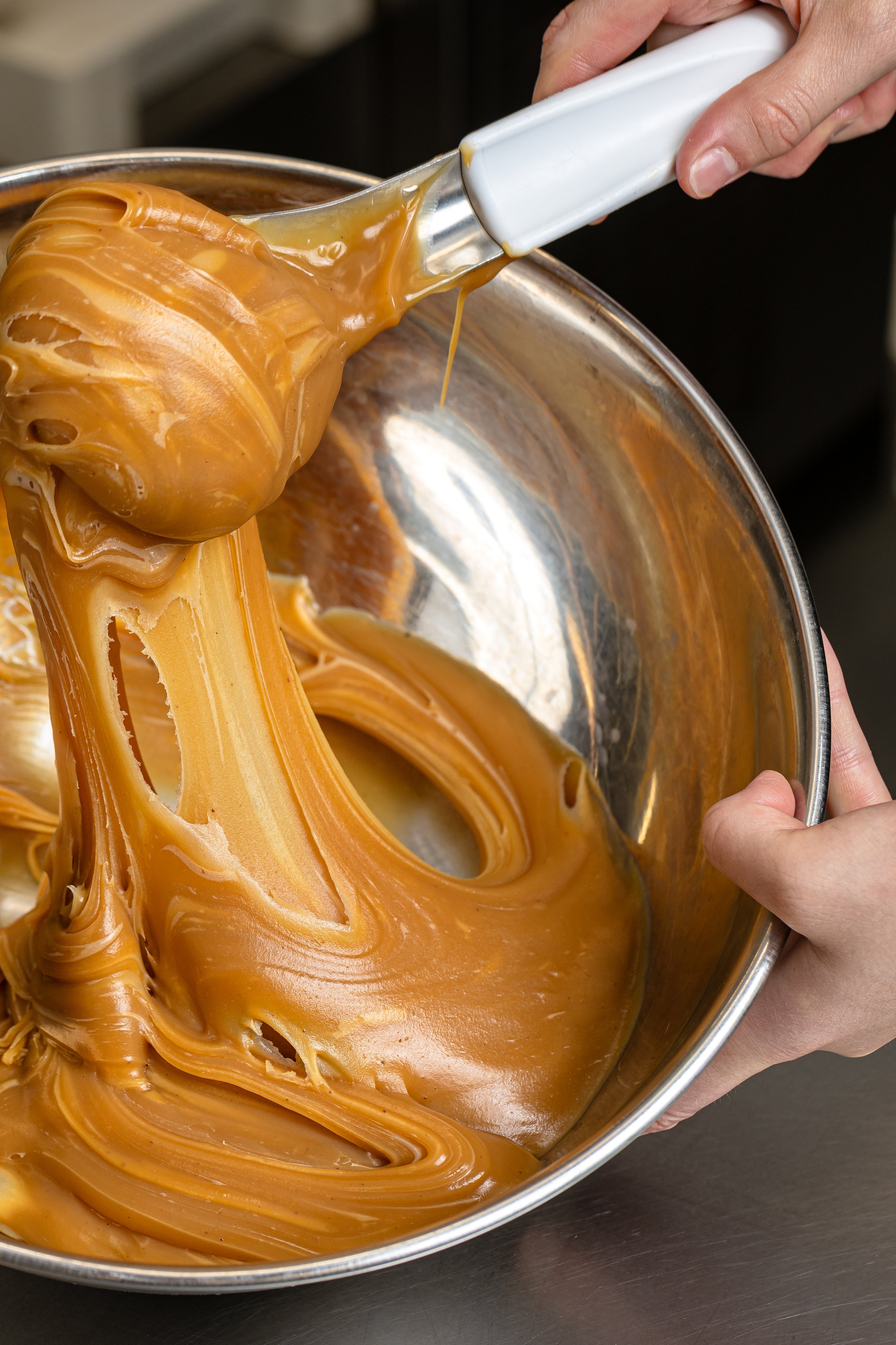Little 'Lato Gelato - A person is using a spatula to lift melted caramel from a mixing bowl, showing its stretchy and smooth texture.