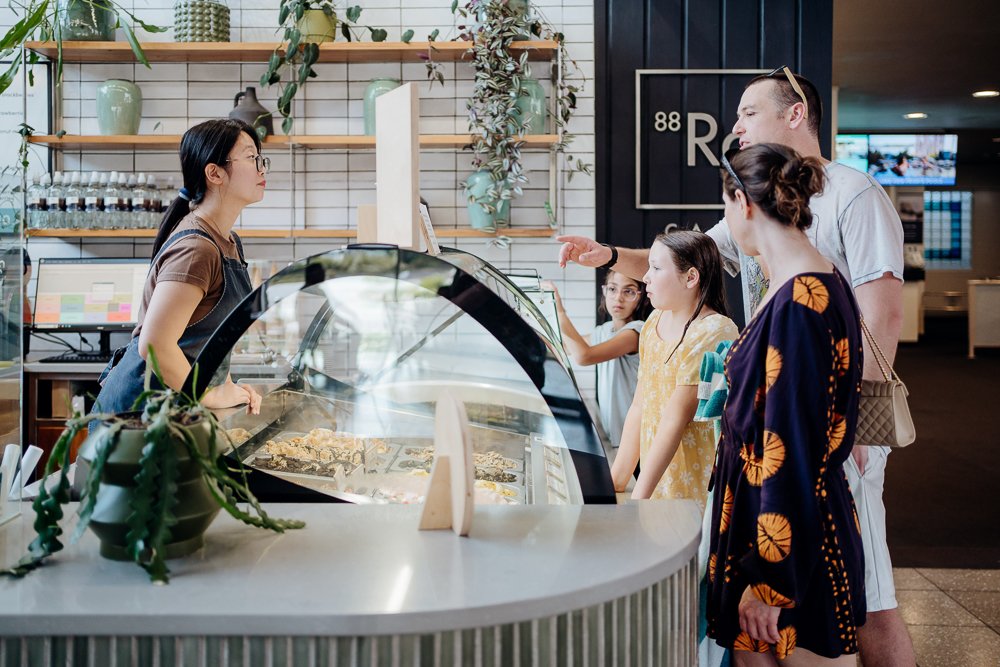 A group of people ordering ice cream at a gelato shop, with a female staff behind the counter serving them.