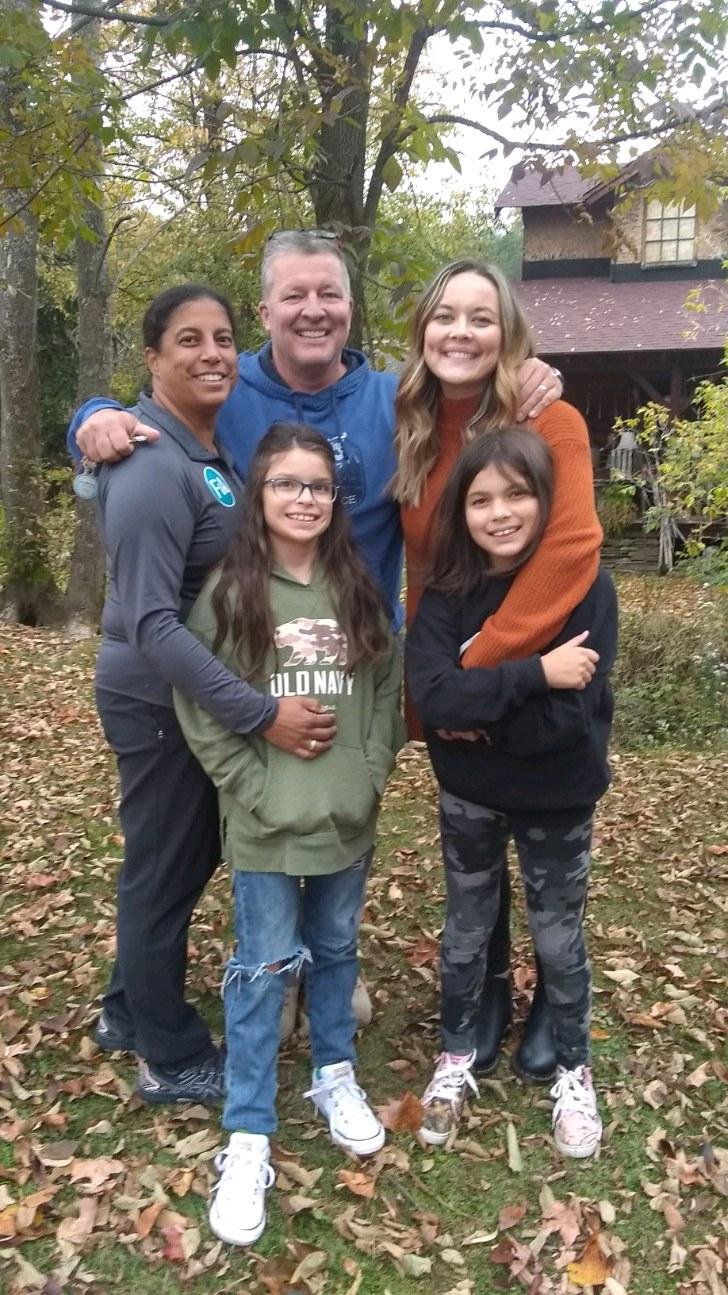 Cristina Moore and her family standing outdoors on a fall day with trees and a house in the background.
