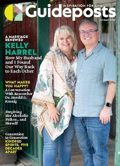 A smiling older woman with blonde hair and a man with short gray hair and glasses standing outdoors in front of a wooden fence, posing for a photo on the cover of Guideposts magazine. The woman is dressed in a patterned shawl, and the man is wearing a light blue shirt and jeans.