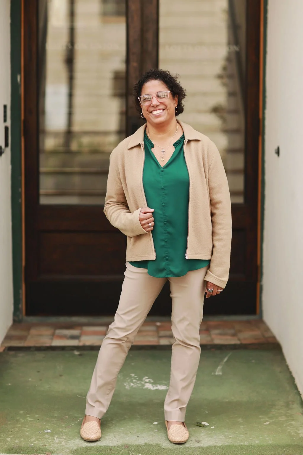 Cristina Moore, a faith-based author and speaker, wearing glasses, in green blouse, beige jacket, beige pants, standing in front of door.