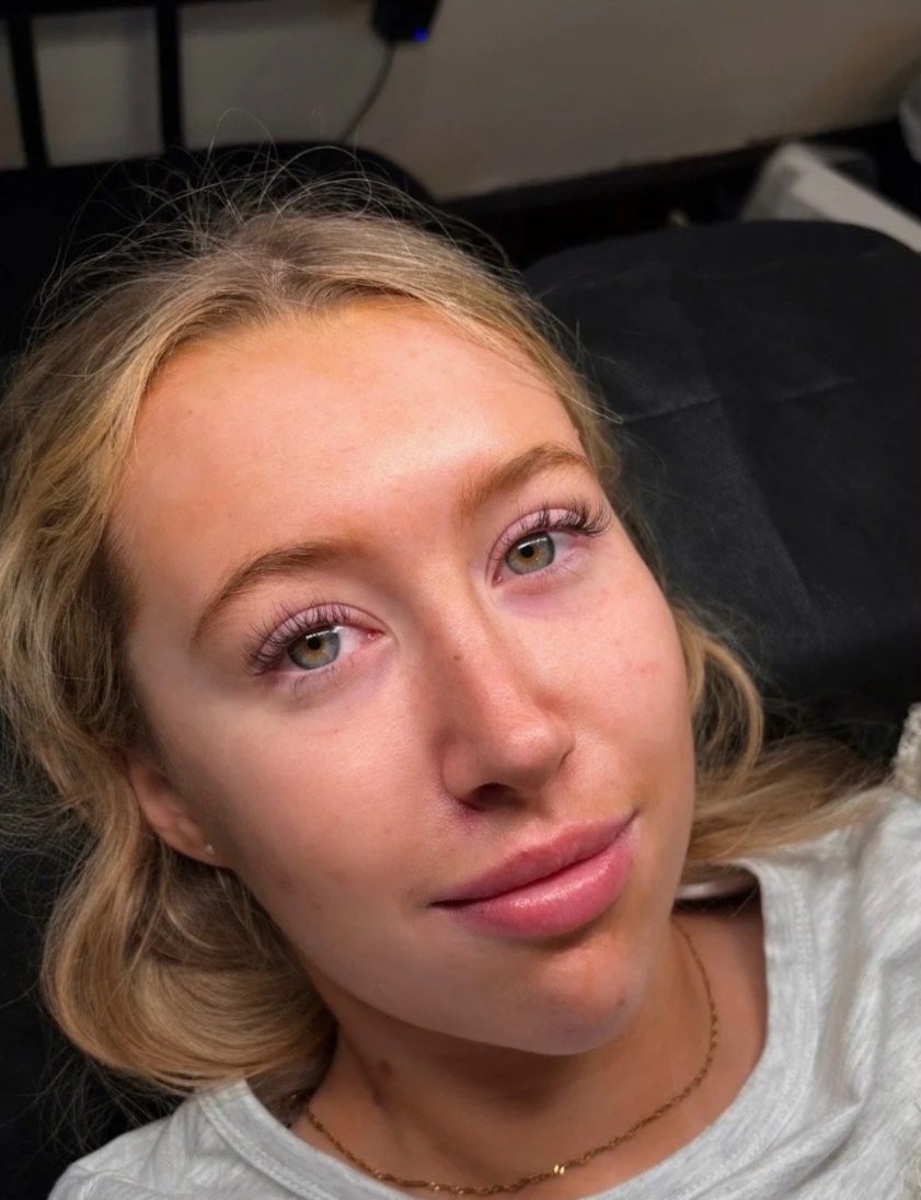 A young woman with light brown hair lying on a black surface, looking up at the camera, with a neutral expression.
