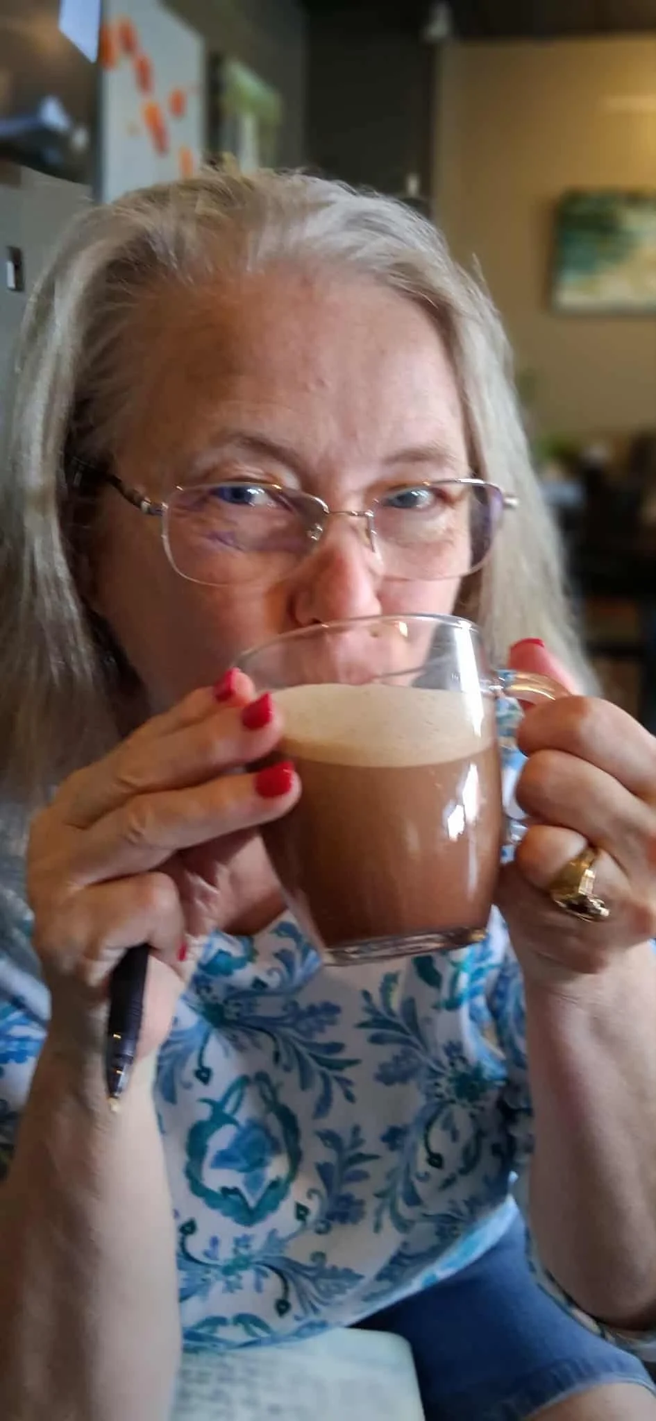 Woman with glasses and red nails holding a mocha, sitting indoors.