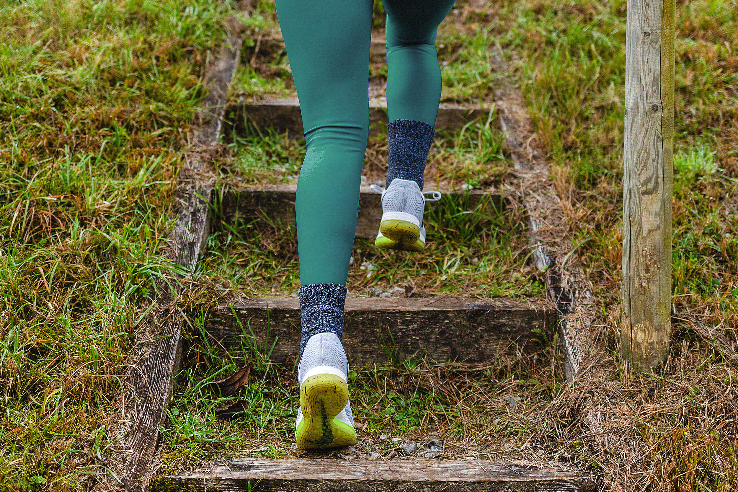 Person klettert eine Holztreppe im Freien, umgeben von Gras und natürlichen Elementen.
