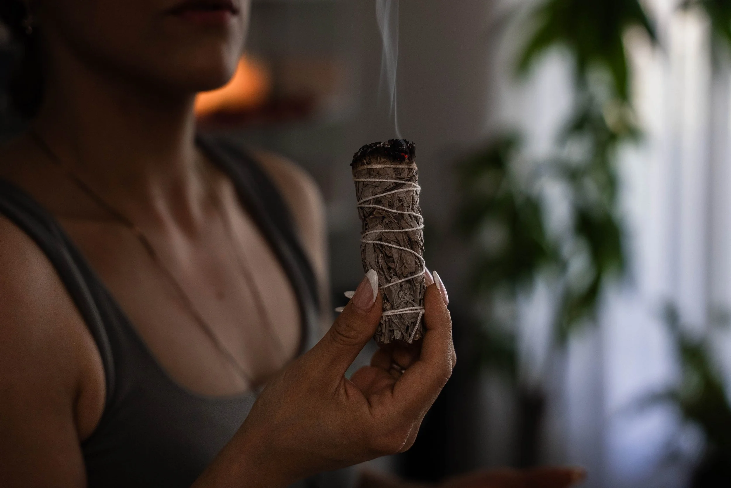 A woman is holding a burning sage bundle with smoke rising from the top.