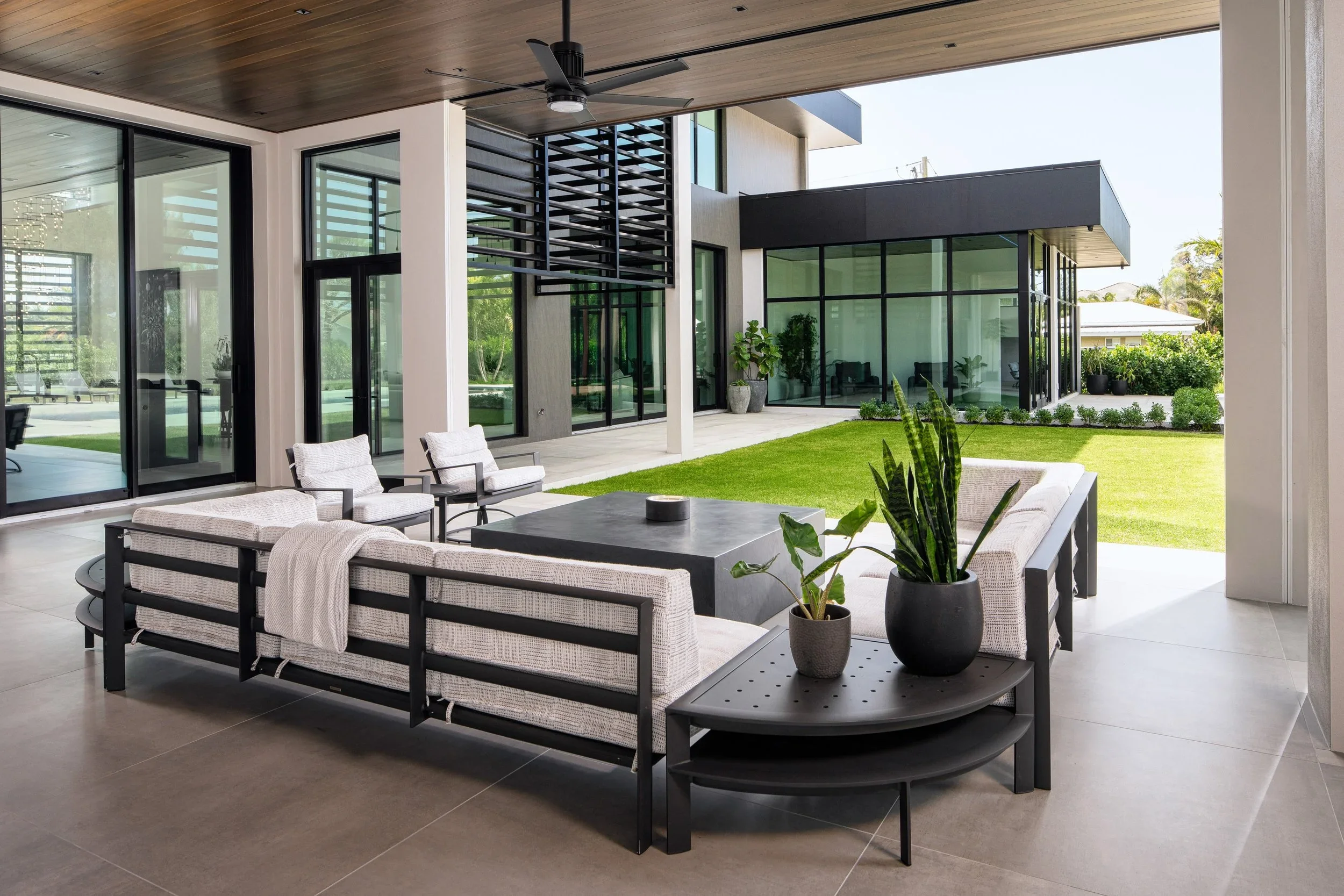 Modern outdoor patio with seating area, glass walls, and a view of a green lawn and garden.