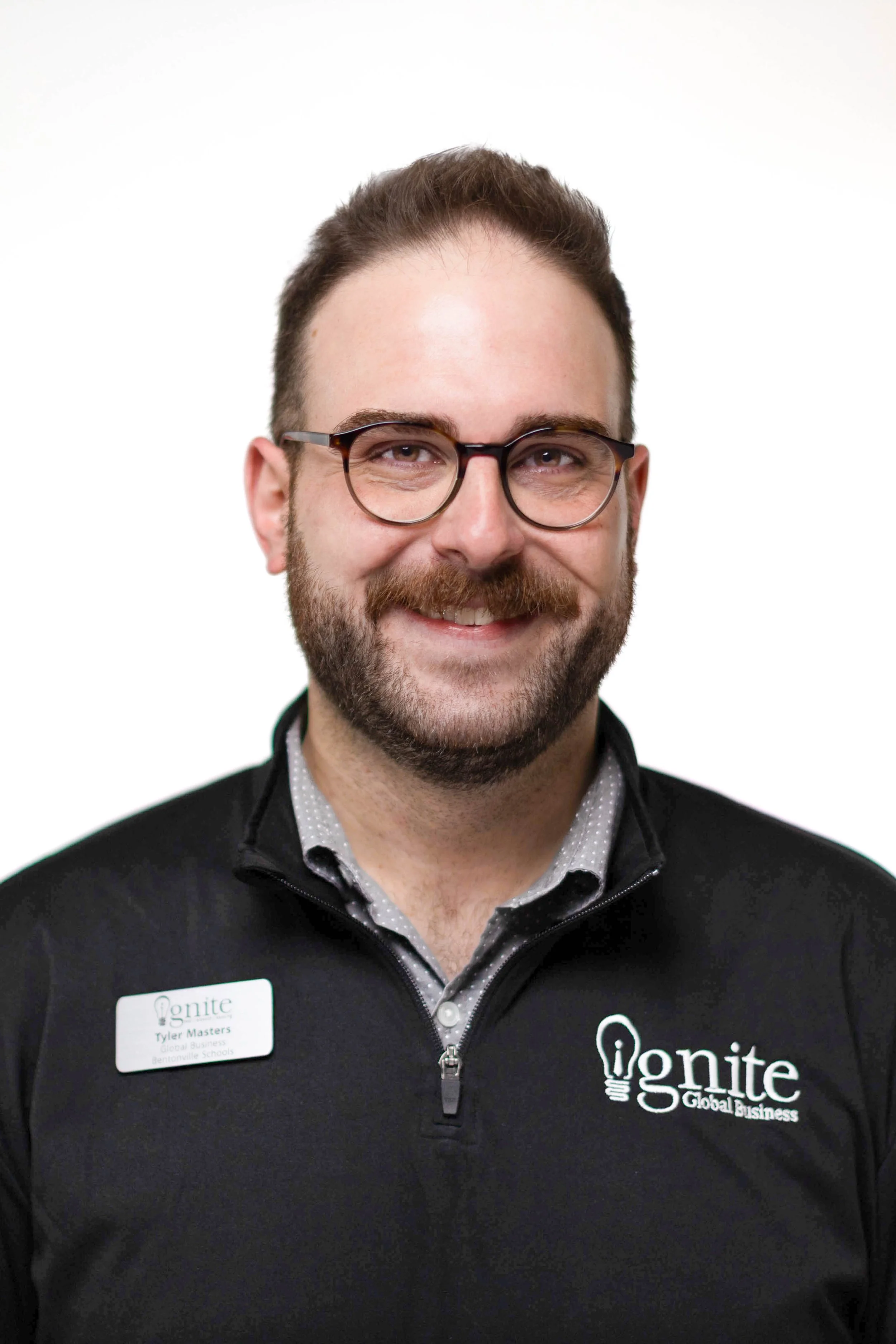 Man wearing glasses and a black jacket with a logo that says 'ignite Global Business' and a name tag that reads 'Tyler Masters'.