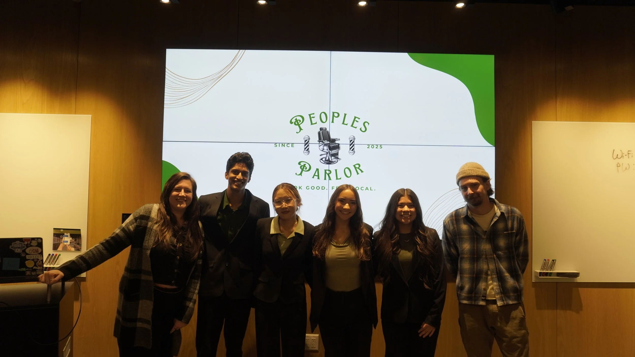 Group of six people standing in front of a large digital screen displaying 'Peoples Parlor' logo at an indoor event.