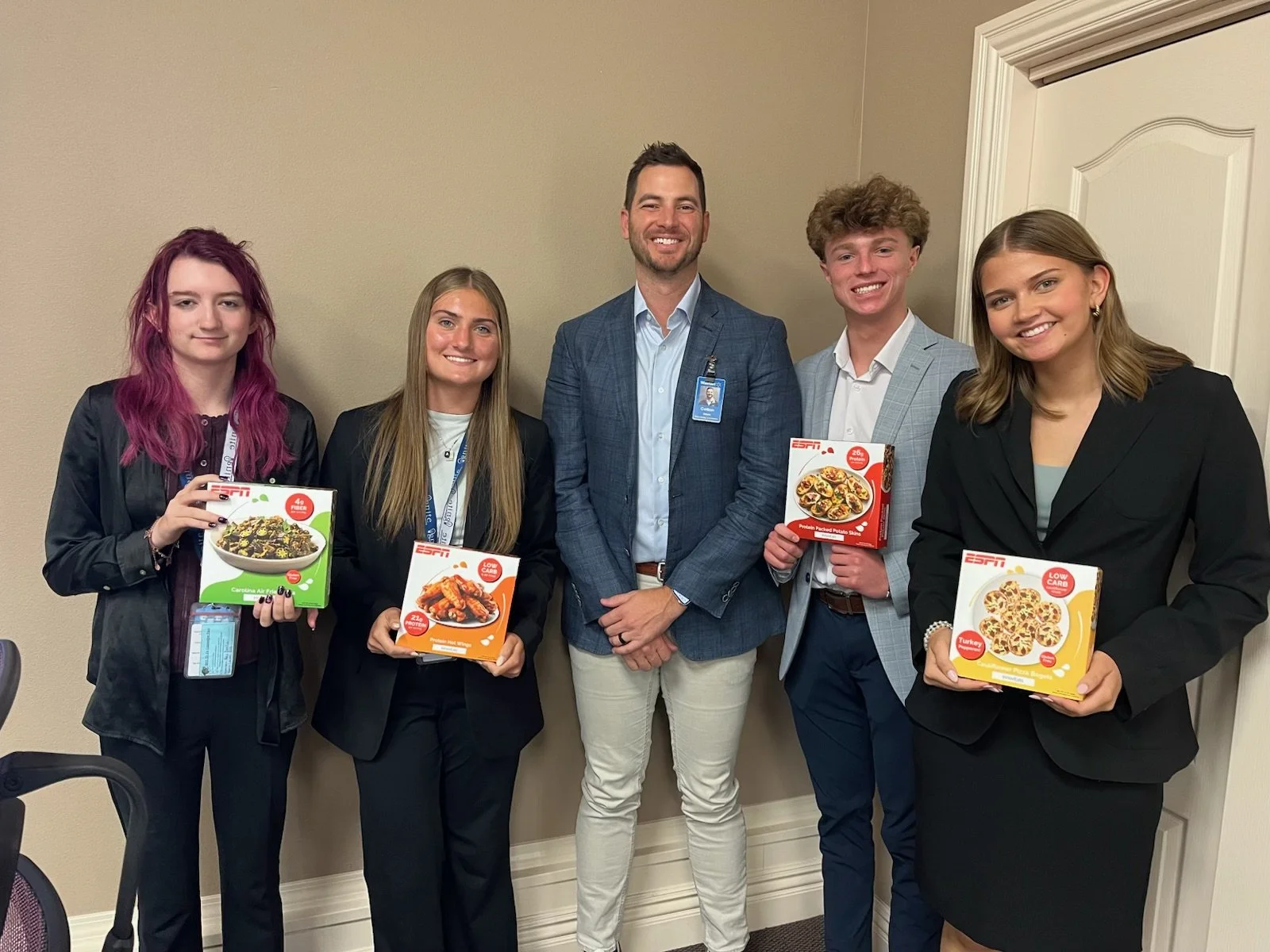 Group of five people in business attire standing inside, holding various frozen meal boxes, smiling at the camera.