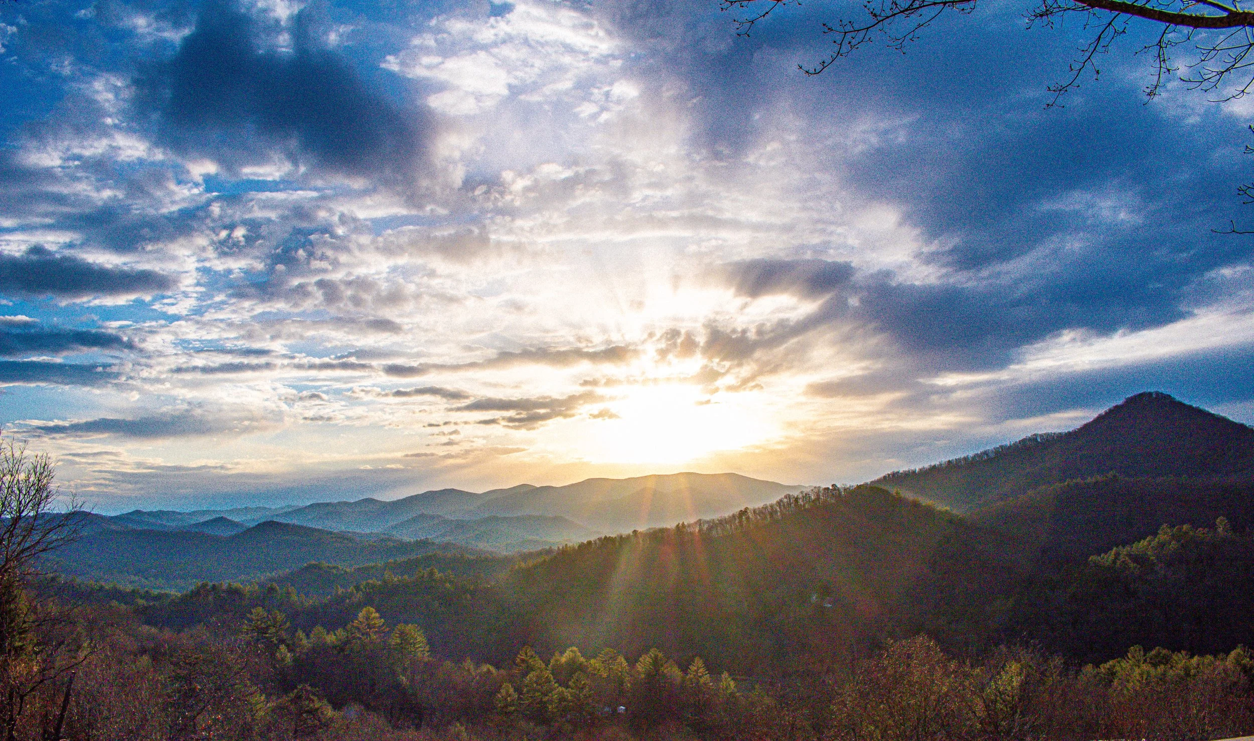 Sunset over a mountain range with clouds in the sky and sunrays shining through