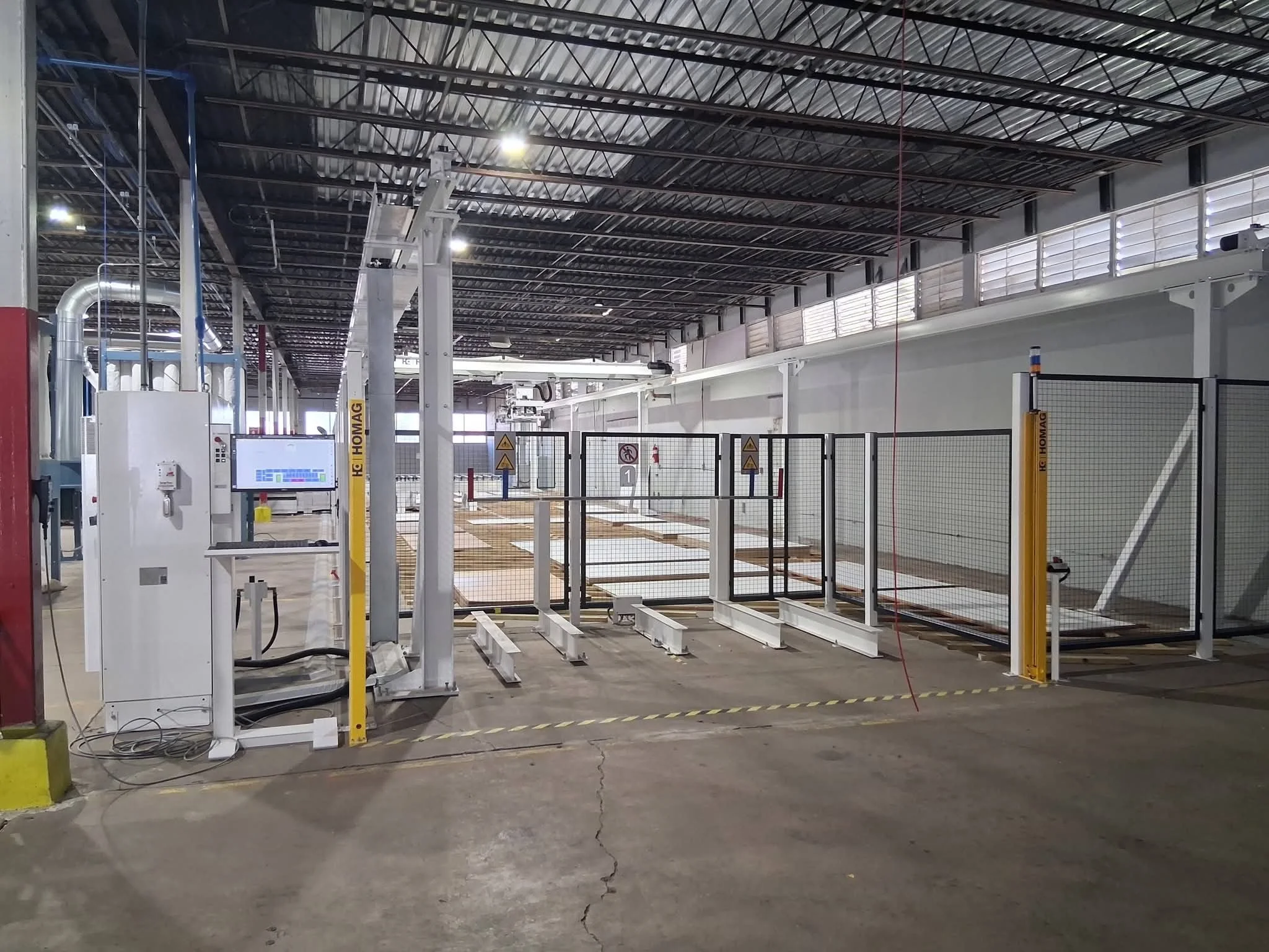 An industrial or warehouse environment with a gated area, safety signs, and machinery, under a high ceiling with metal beams.