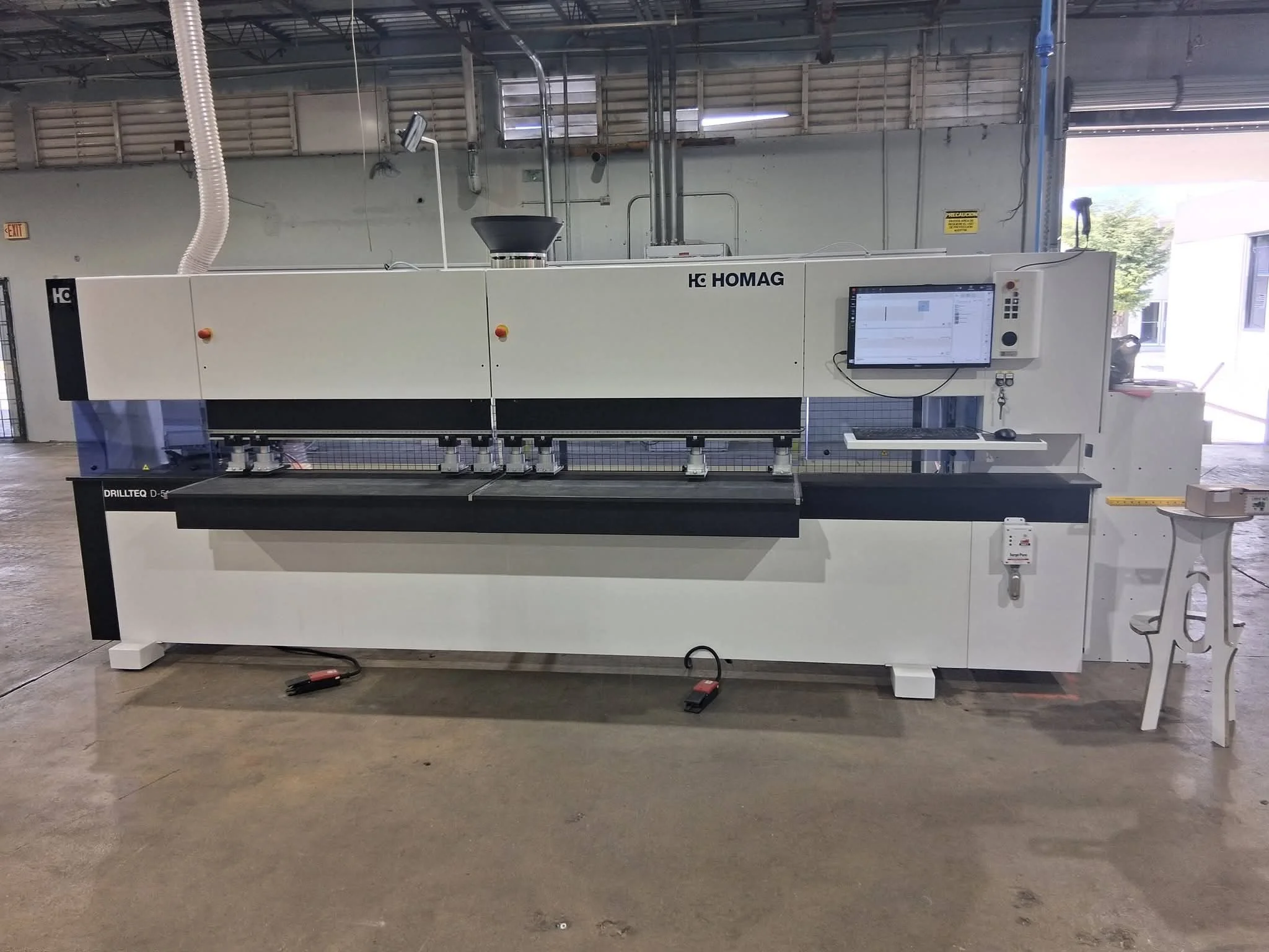 Industrial machine in a factory with computer screen and various controls, labeled Homag, with a work surface in the foreground and equipment in the background.