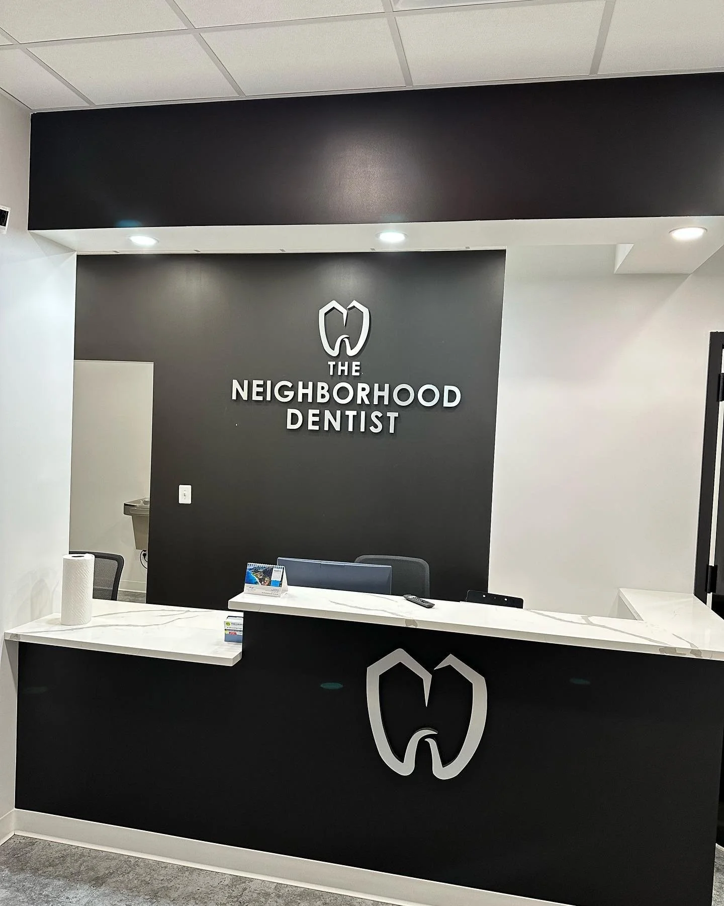 Reception desk at The Neighborhood Dentist office with a dental logo and sign on the black wall.