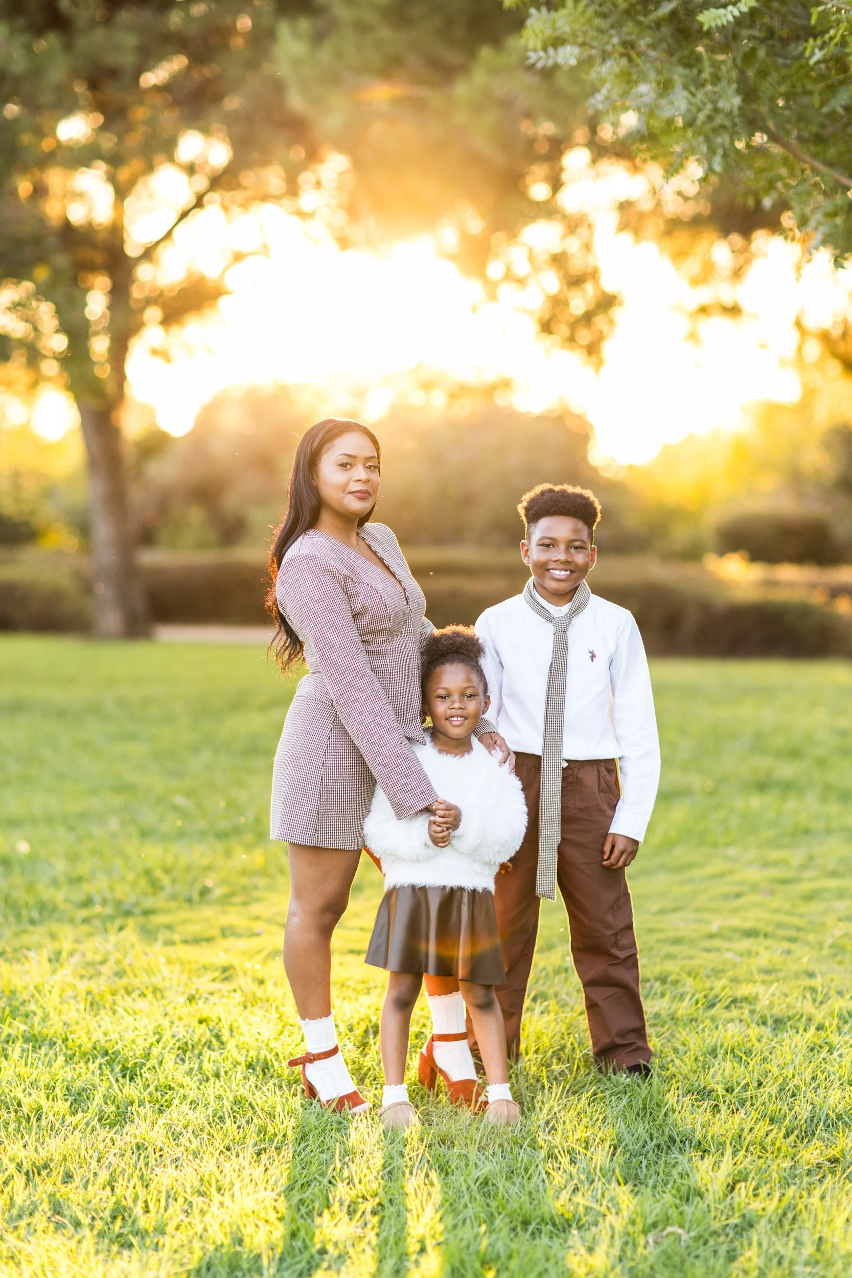 A woman and two children standing on a grassy field at sunset, smiling and holding hands.