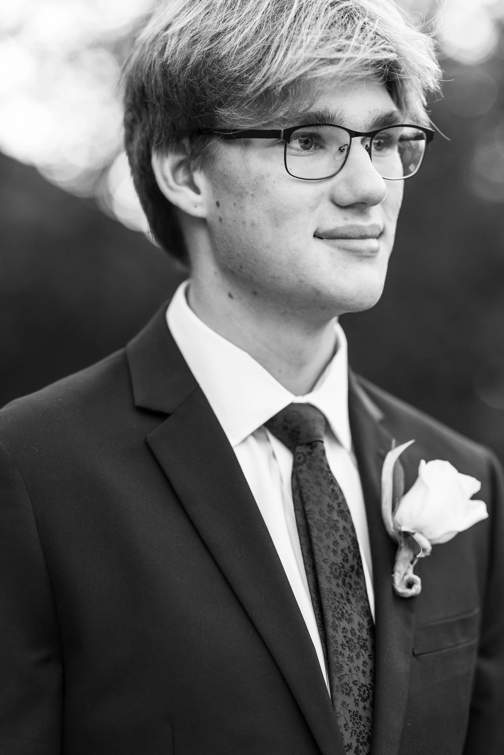 Black and white photo of a young man in a suit and tie with glasses, wearing a boutonniere.