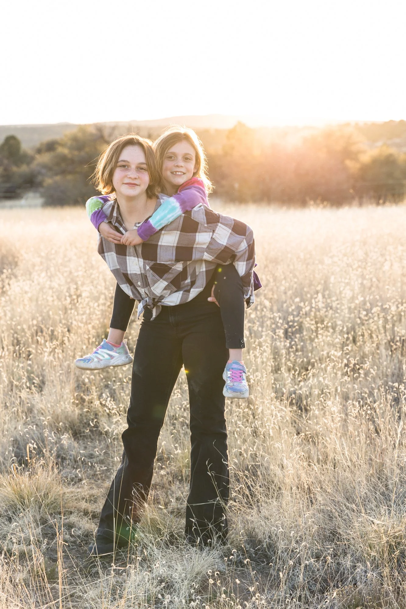 A person carrying a young girl on their back in a grassy field at sunset.