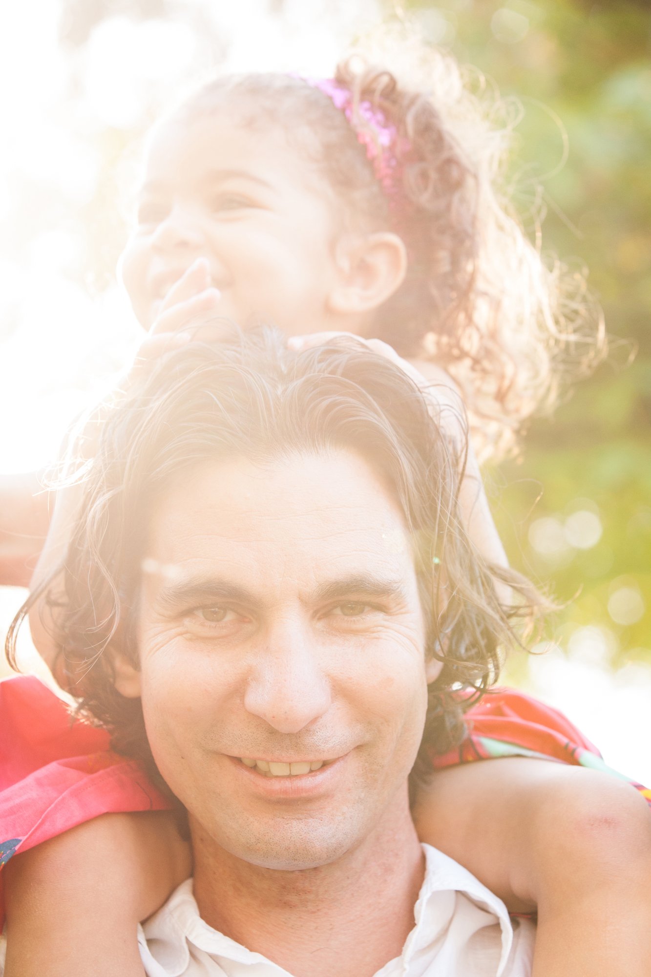 A man giving a girl a piggyback ride outdoors with sunlight creating a bright, warm glow around them.
