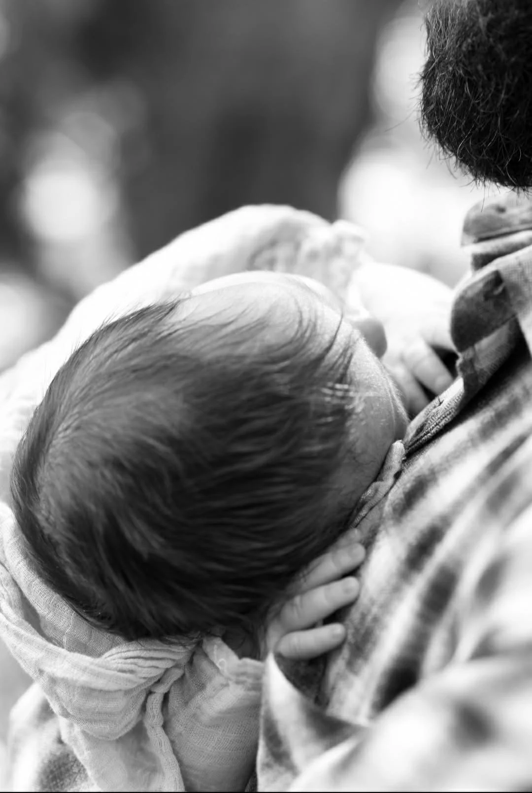 A man holding a sleeping baby close, with the baby's head resting on his chest.