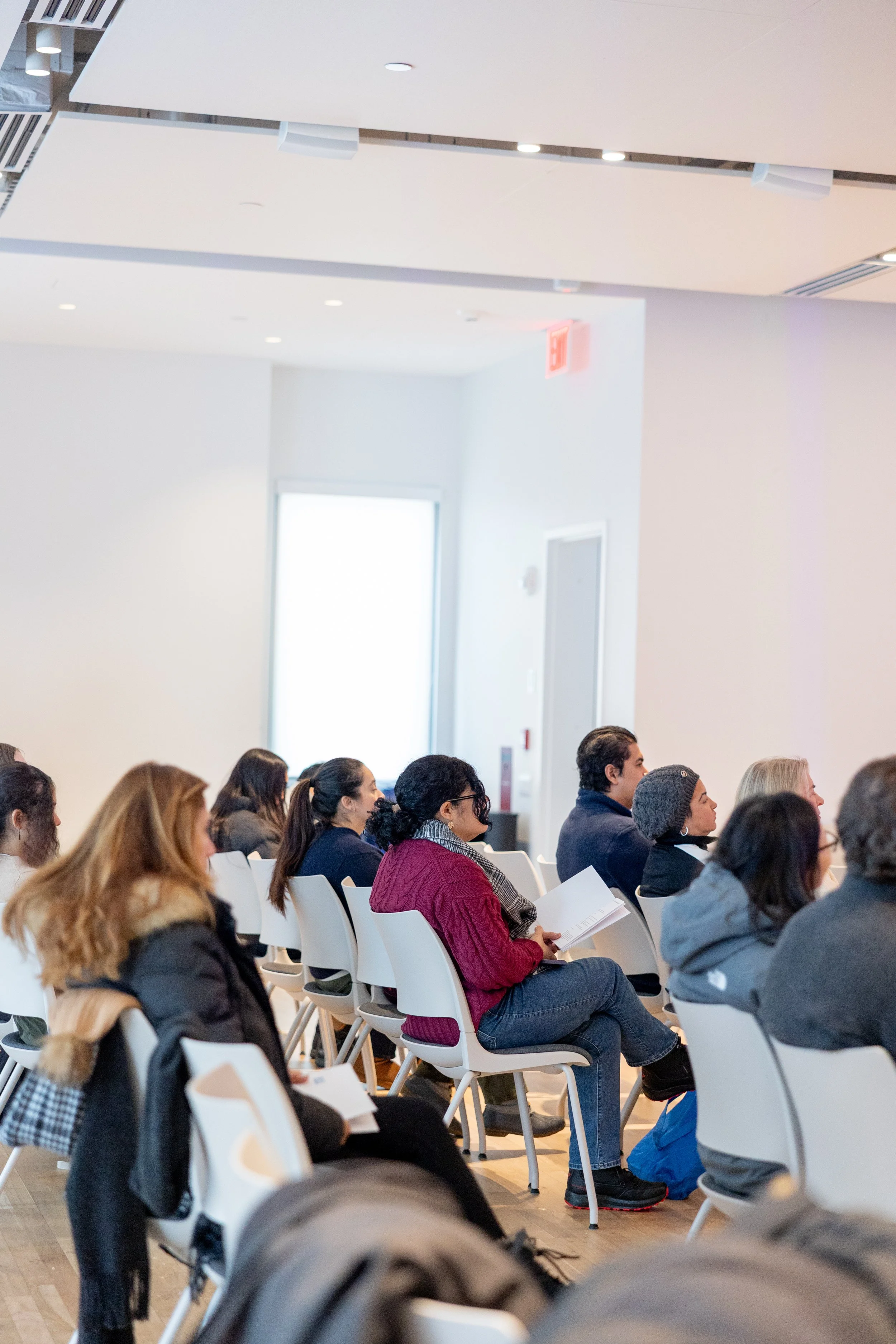 People sitting in chairs attending a presentation or lecture in a bright, modern room.