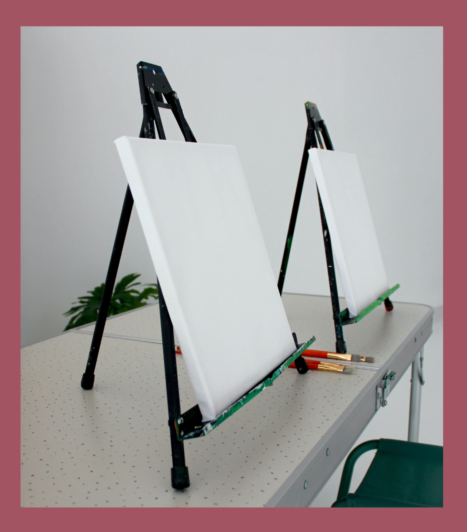Photograph of easles with blank canvas, and paintbrushes sitting next to them on a table.