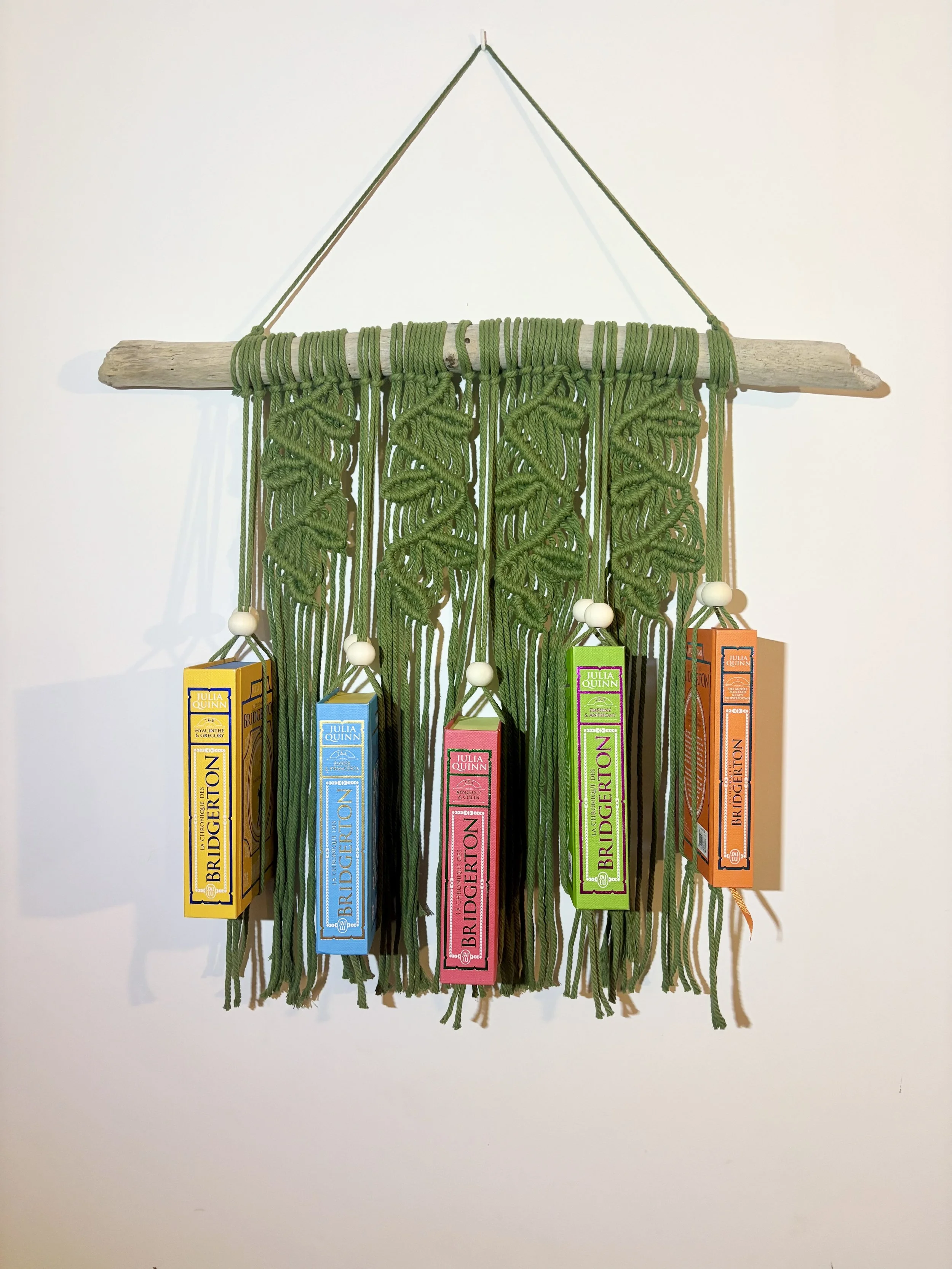 Une décoration murale faite de corde verte, d'un bâton en bois et de boîtes de carton colorées suspendues.