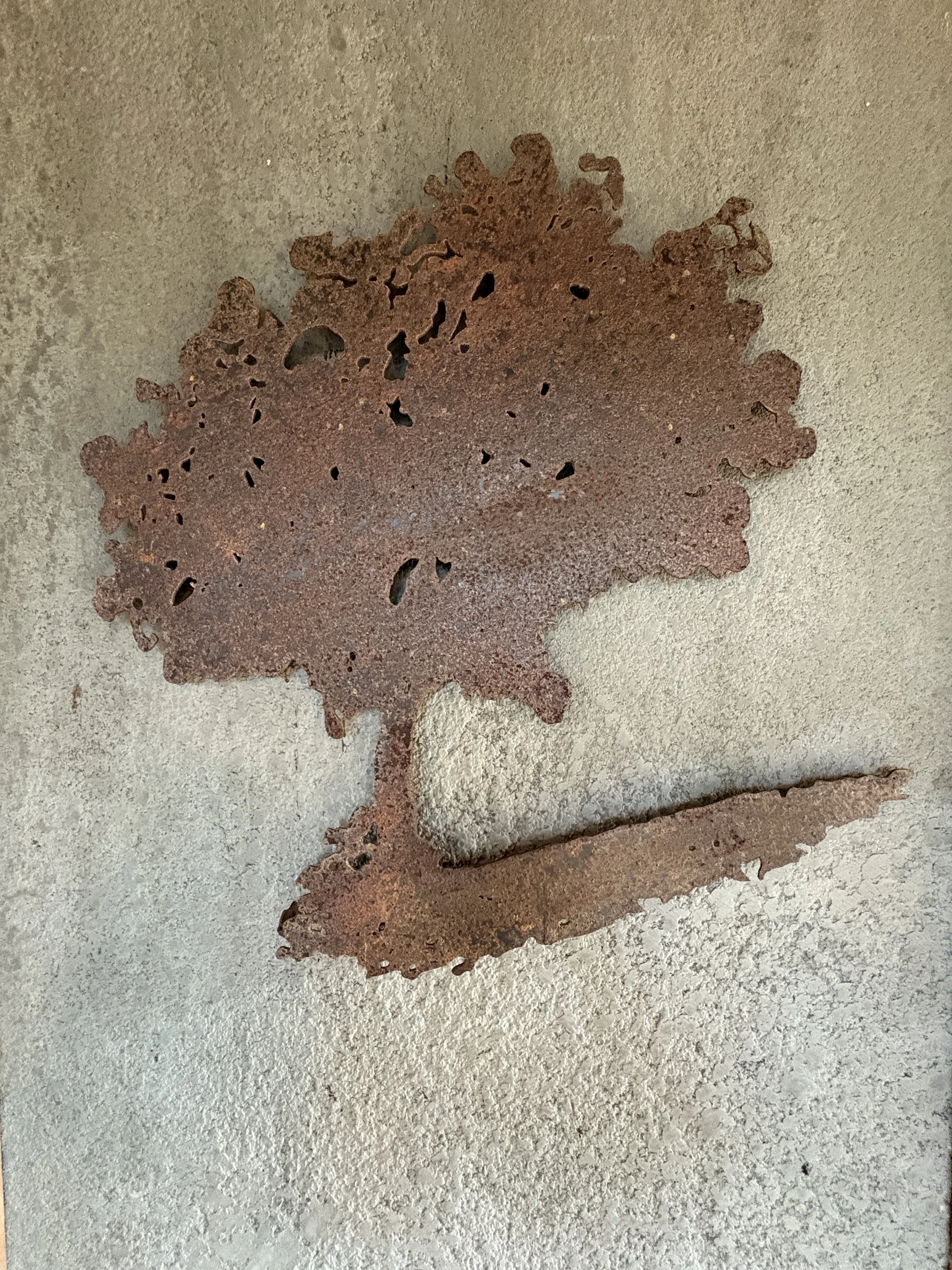 Rusty metal leaf sculpture mounted on a beige wall.